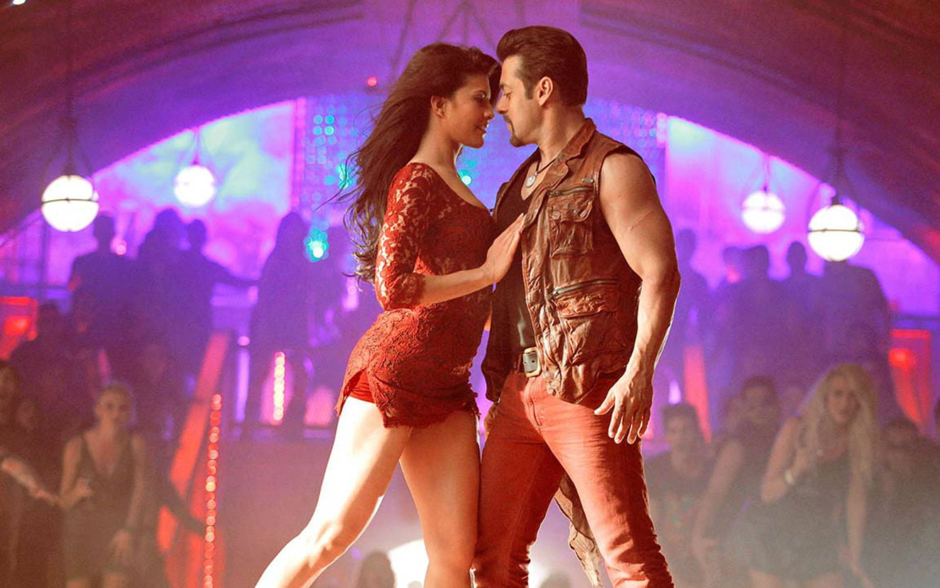 Salman Khan 桌布 壁紙 — 一對情侶在充滿活力的夜總會中親密跳舞，夜總會沐浴在紫色和橙色的燈光中，身後是模糊的派對參與者。