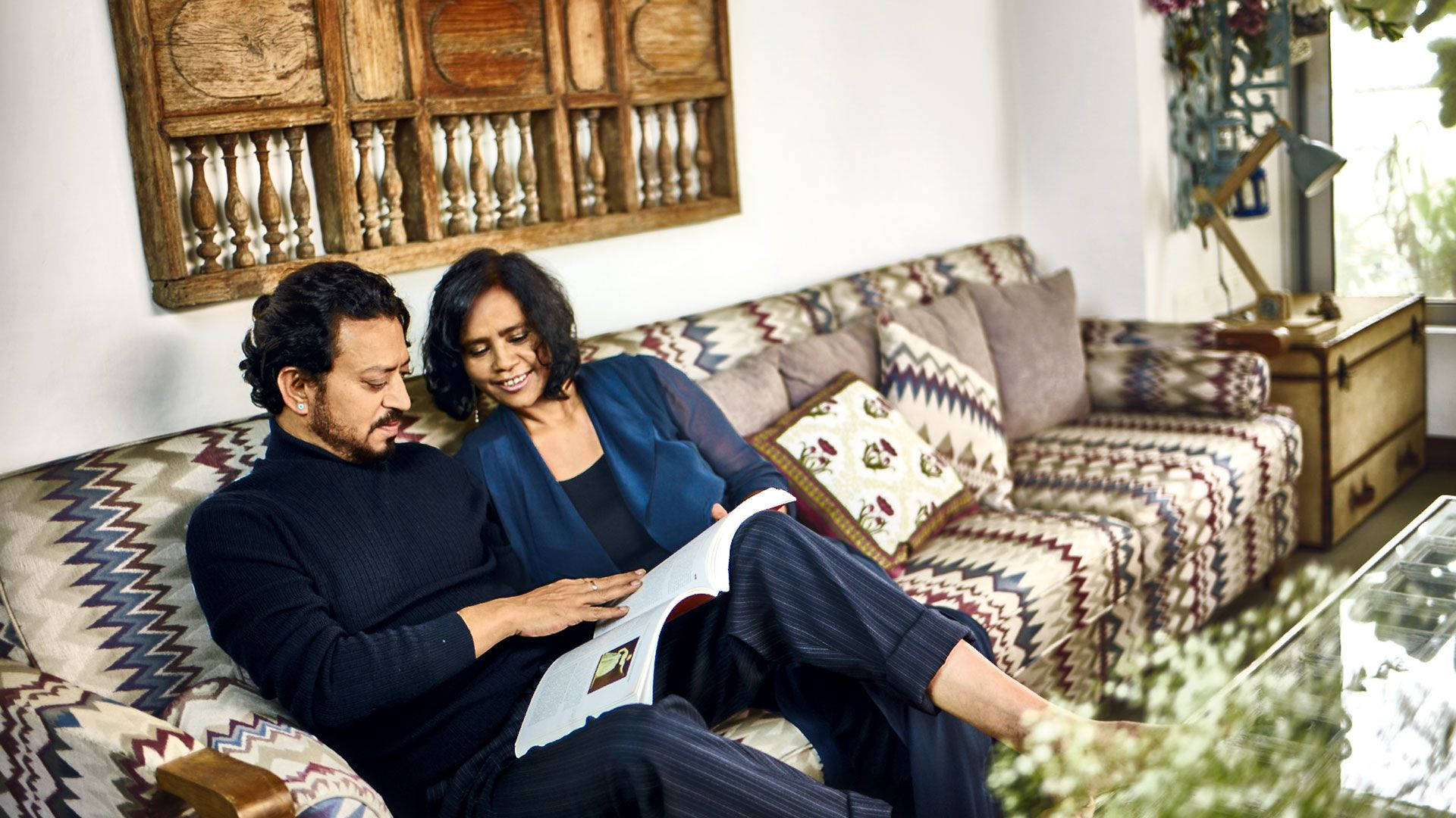 Irrfan Khan 桌布 壁紙 — 一對情侶在圖案沙發上放鬆，一起閱讀一本書，身處溫暖燈光的舒適客廳。