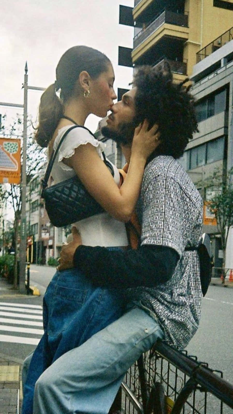 Aesthetic Couple 桌布 壁紙 — 一對情侶在城市的街道上親密接吻，男子將女子抱起並靠在欄杆上。