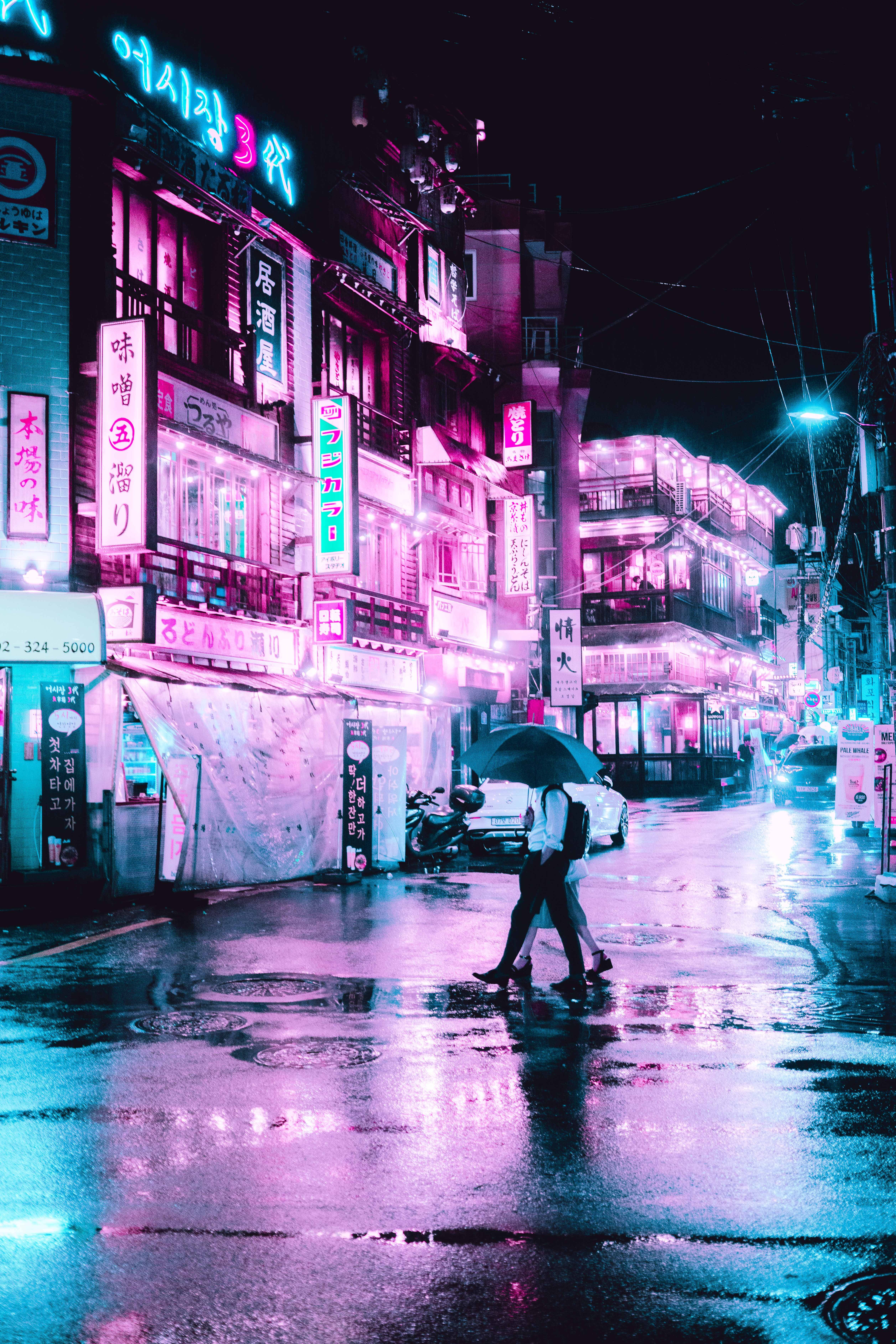 手機 桌布 壁紙 — 一對情侶在夜晚撐著傘走過霓虹燈閃爍、雨水浸濕的城市街道，反射出鮮豔的粉紅色和藍色燈光。