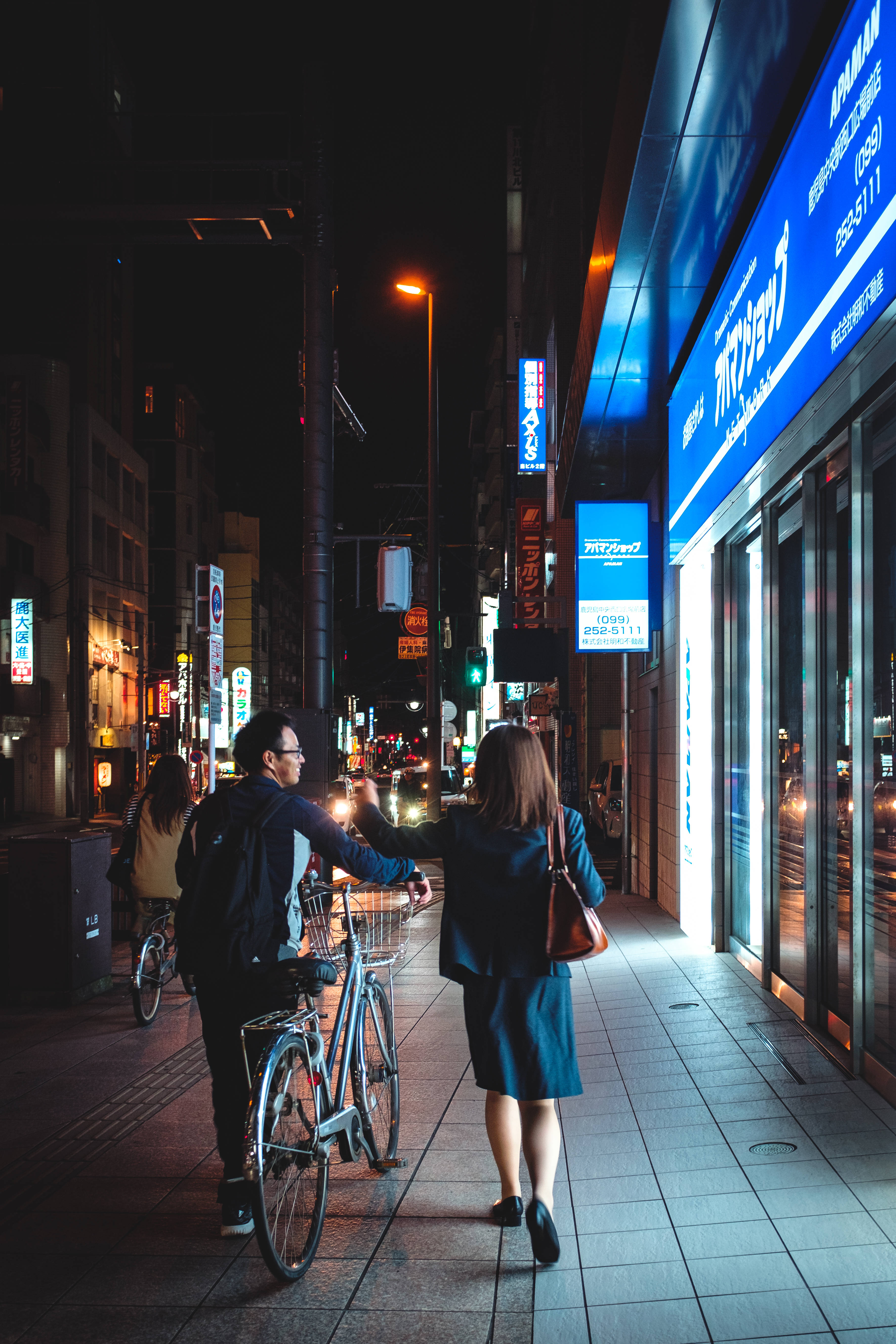 lights 桌布 壁紙 — 一對情侶在夜晚沿著霓虹燈閃爍的東京街道行走，帶著一輛腳踏車，一隻手伸出觸摸另一隻手