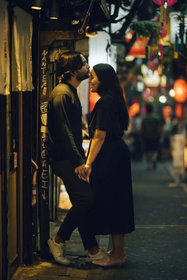情侶 桌布 壁紙 — 一對情侶在夜晚溫暖燈光照亮的東京狹窄小巷中牽手微笑，分享親密時刻。