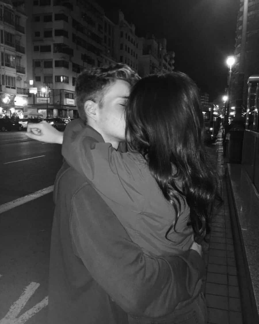 Boyfriend And Girlfriend 桌布 壁紙 — 一對情侶在夜晚的城市人行道上熱情擁抱的黑白照片，背景有街燈和建築物。