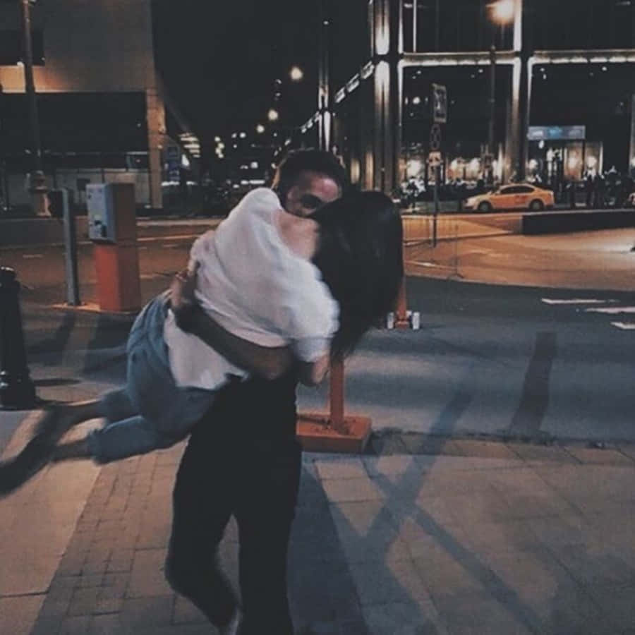 Cute Boyfriend 桌布 壁紙 — 一對情侶在夜間溫暖街燈下的城市人行道上熱情擁抱，背景是模糊的城市景觀。