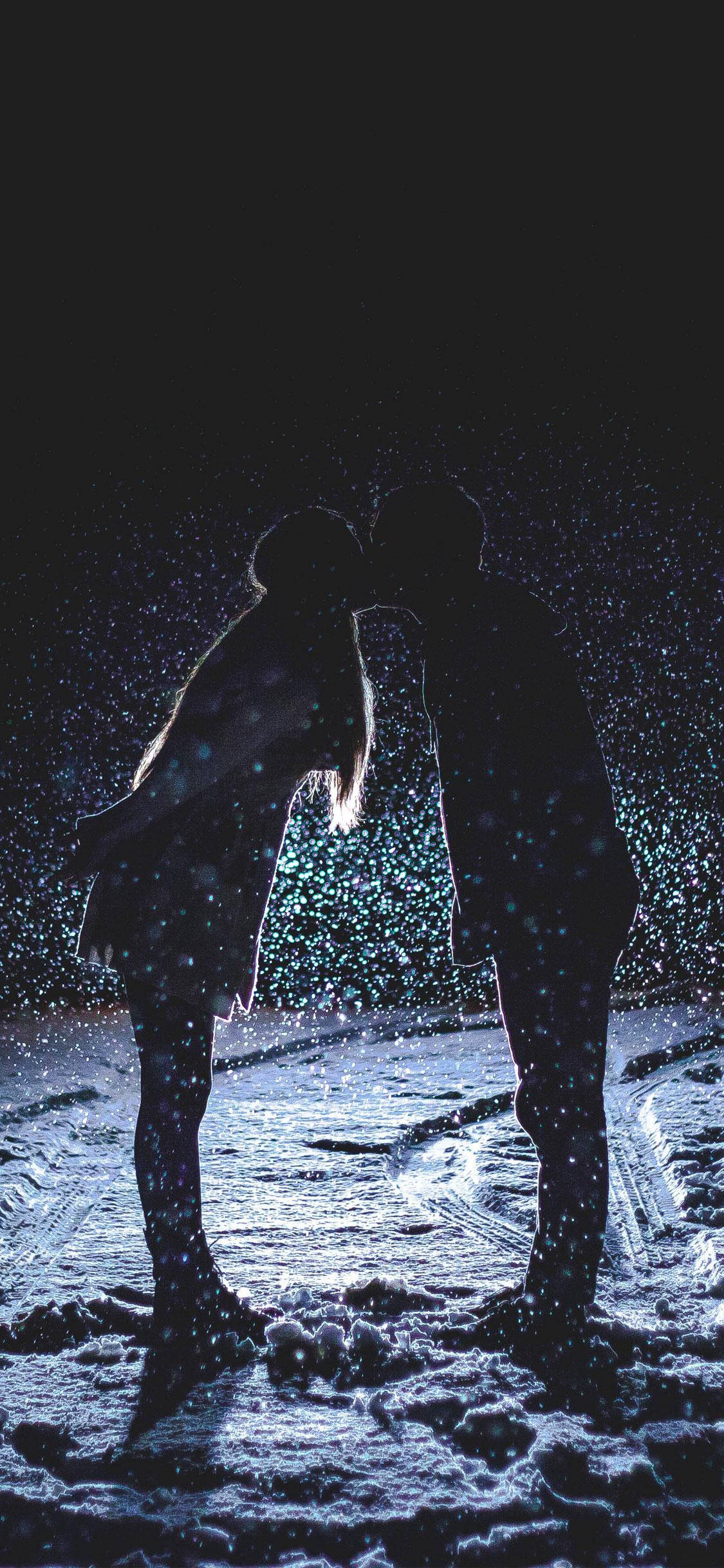 Love iPhone 桌布 壁紙 — 一對情侶在夜間飄雪下接吻的浪漫剪影，周圍有發光的粒子。