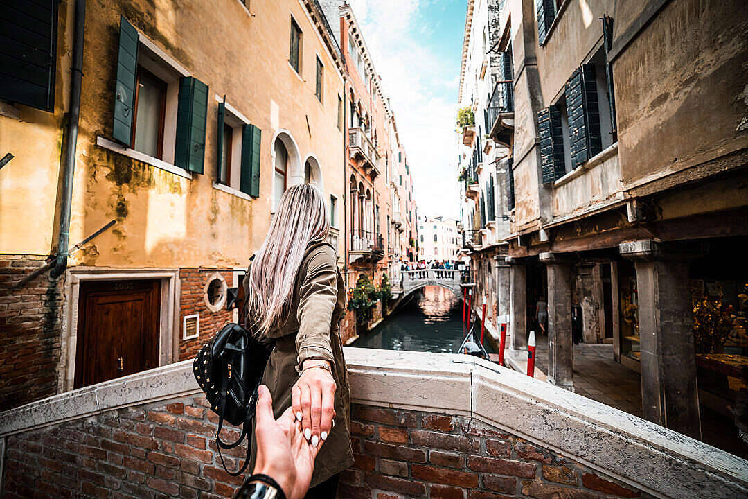 Romantic Couples 桌布 壁紙 — 一對情侶在威尼斯橋上手牽手，俯瞰著狹窄的運河，兩旁是歷史建築，天空明亮。