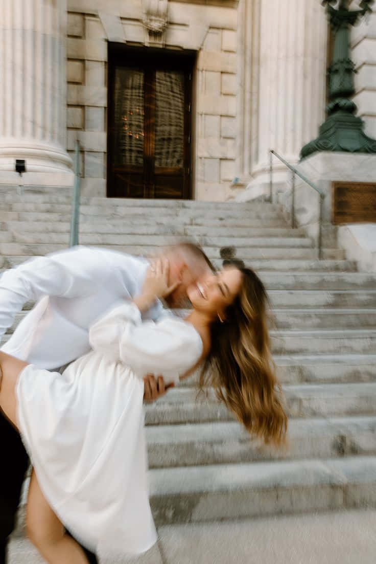 Kissing 桌布 壁紙 — 一對情侶在宏偉古典建築前的石階上分享一個快樂的吻，動態模糊傳達了浪漫和動感。