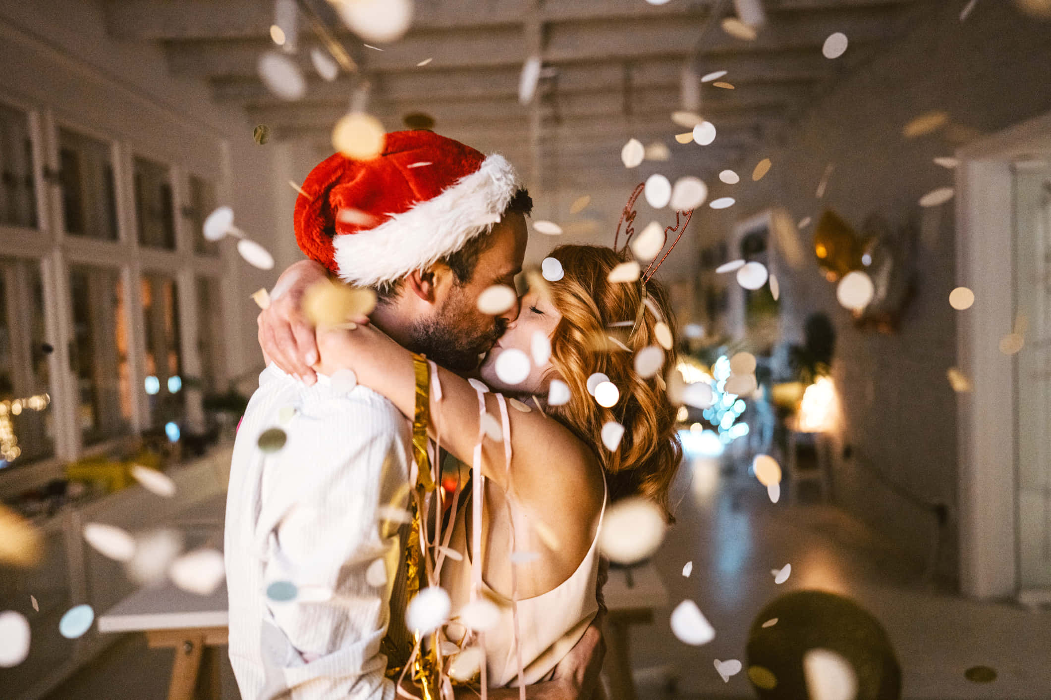 Couples Christmas 桌布 壁紙 — 一對情侶在室內節慶氛圍中熱情接吻，周圍飄浮著五彩紙屑和彩帶。