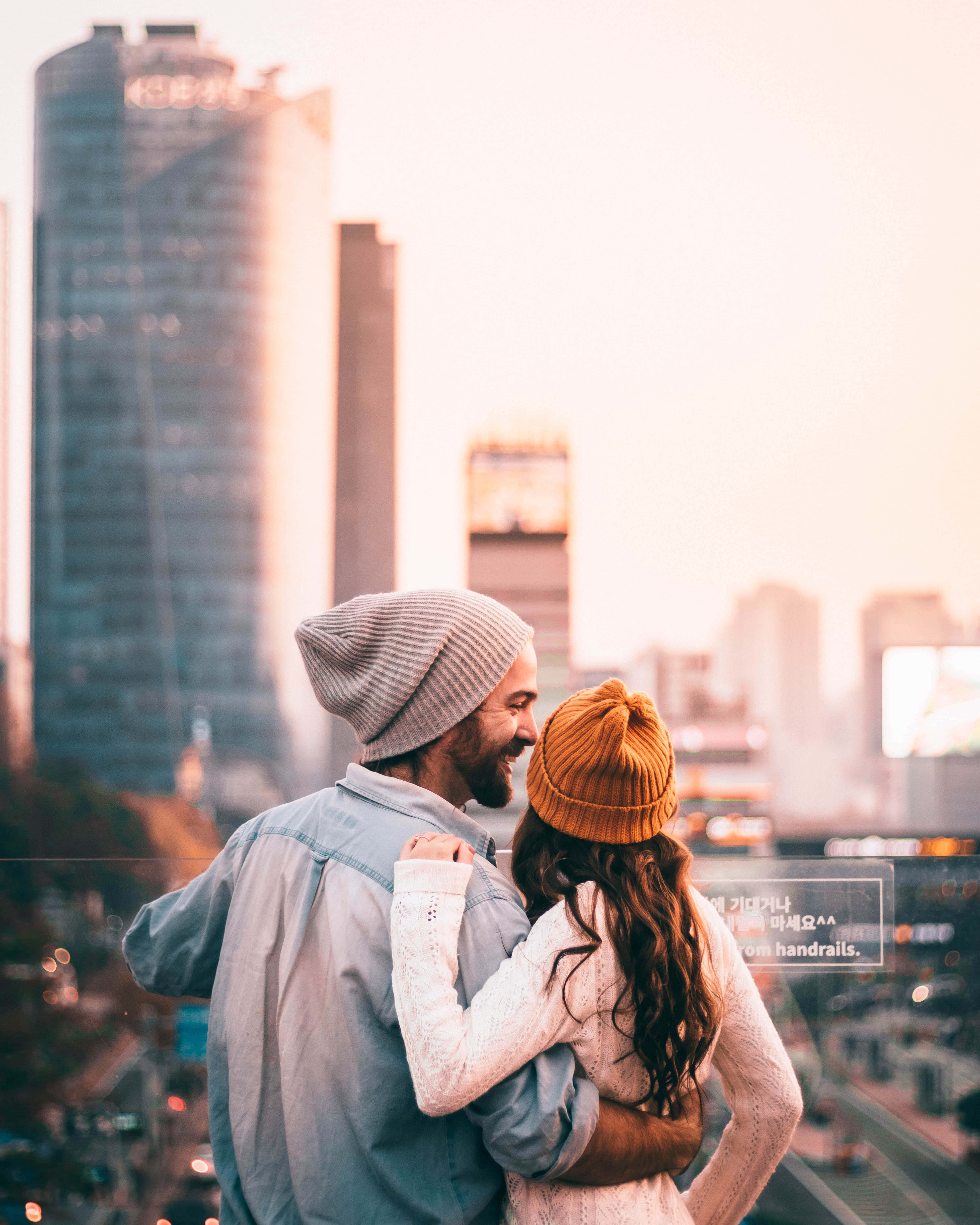 Relationship 桌布 壁紙 — 一對情侶在屋頂上擁抱，俯瞰日落時分閃耀的城市景觀。