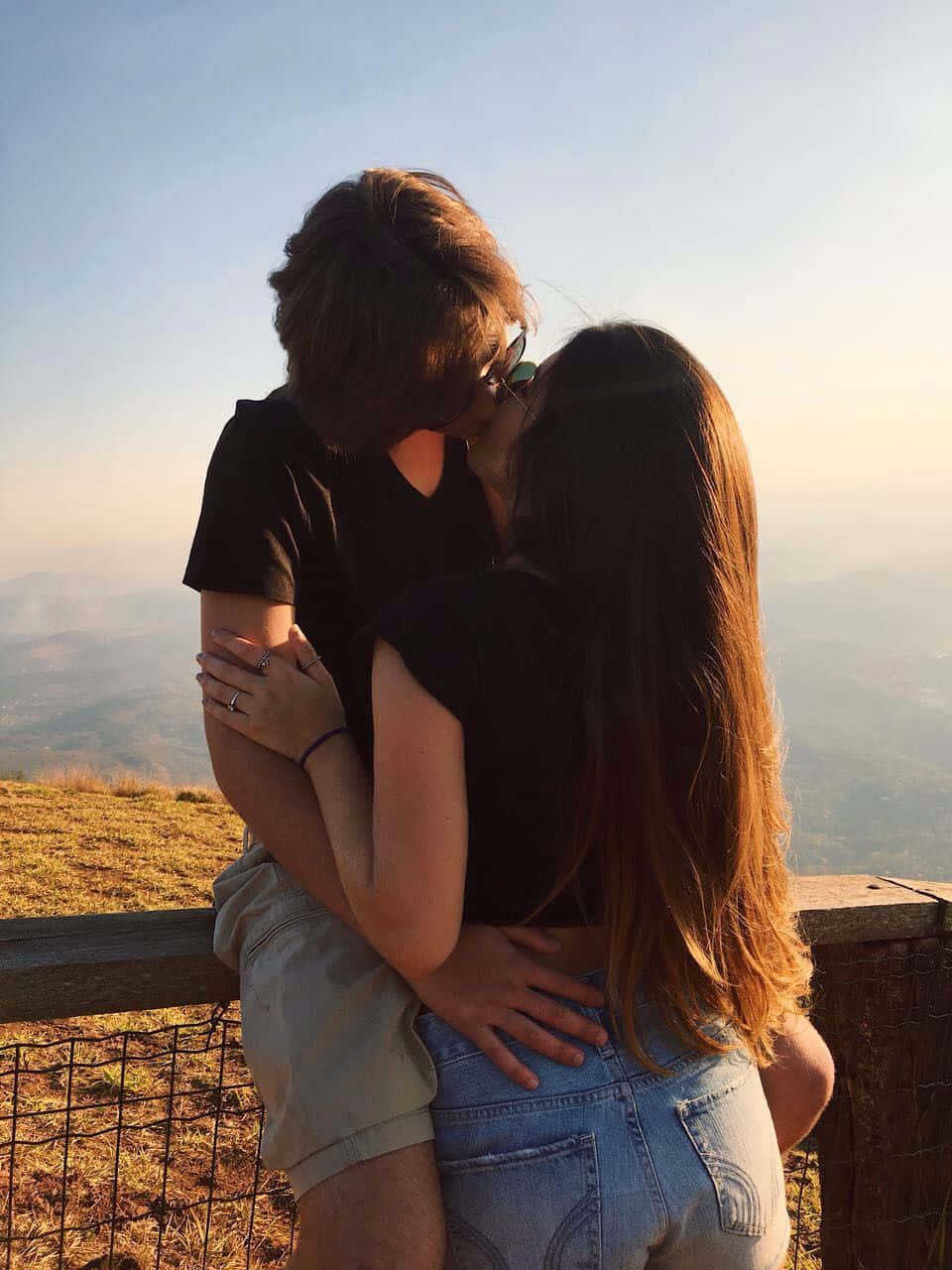boyfriend 桌布 壁紙 — 一對情侶在山頂上擁抱親吻，俯瞰夕陽下煙霧瀰漫的山谷。