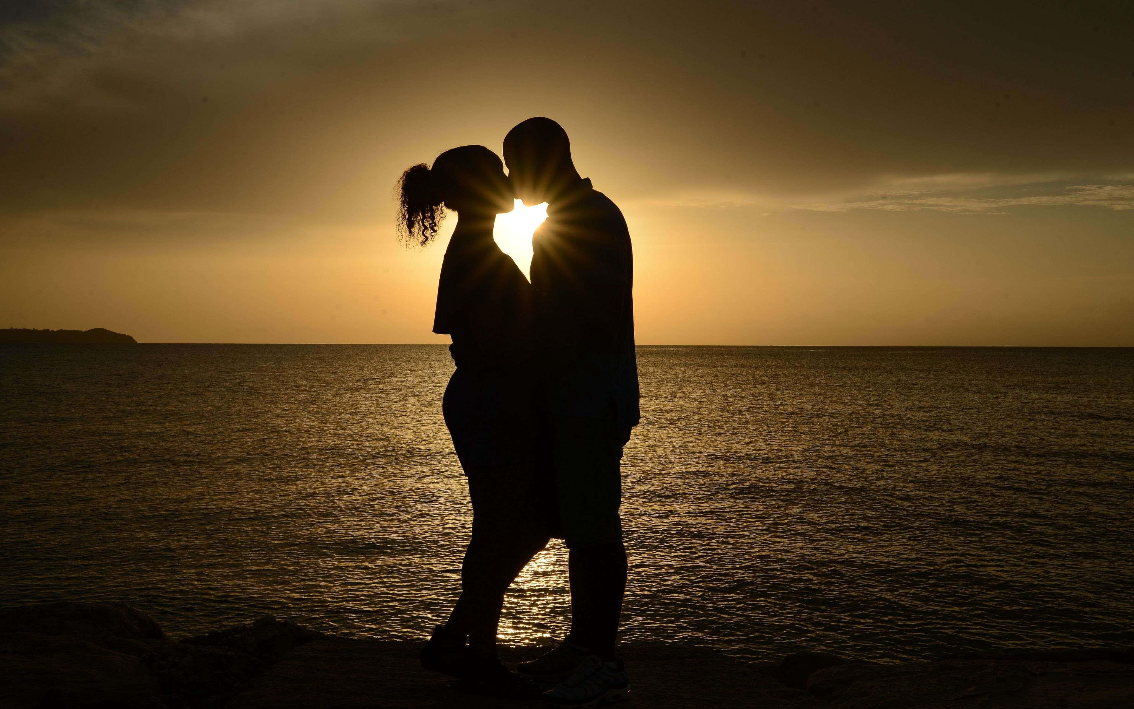 couple love 桌布 壁紙 — 一對情侶在平靜海面上閃耀的日落背景下以剪影接吻。