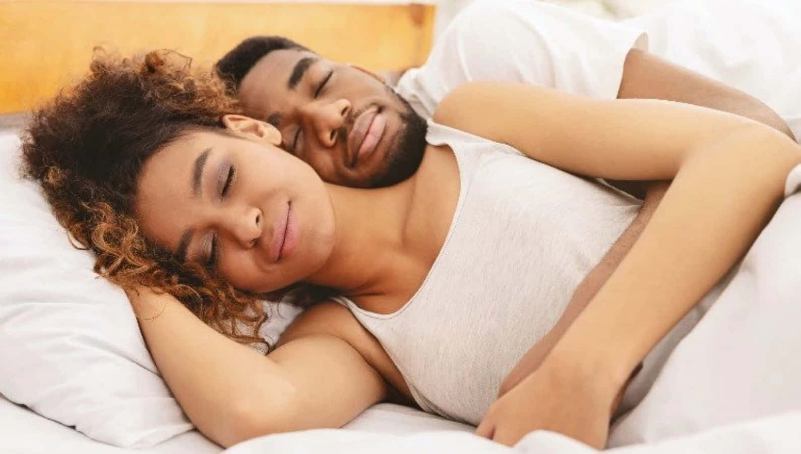Cuddle 桌布 壁紙 — 一對情侶在床上安寧地睡覺，配有柔軟的白色床單和溫暖的木製床頭板。