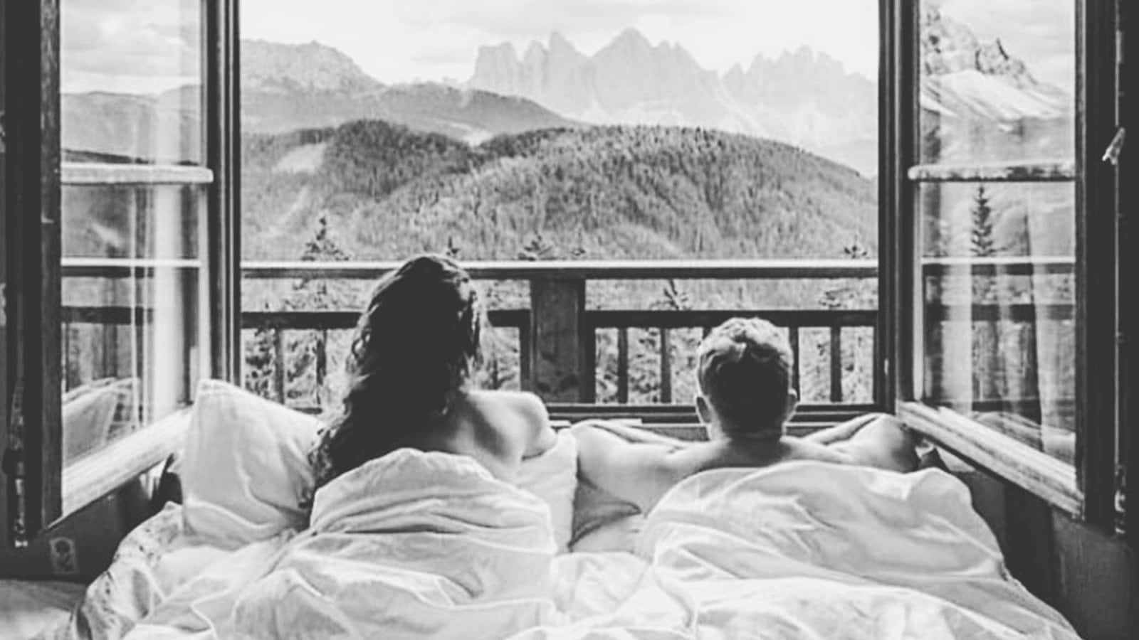 Relationship 桌布 壁紙 — 一對情侶在床上透過窗戶凝視著雄偉的雪山和森林覆蓋的山谷，黑白風格。