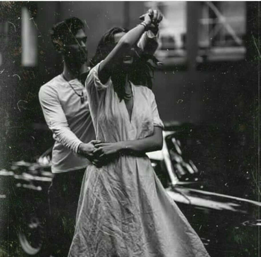 Aesthetic Couple 桌布 壁紙 — 一對情侶在復古車的陰影下親密跳舞的黑白照片，帶有底片顆粒和刮痕。