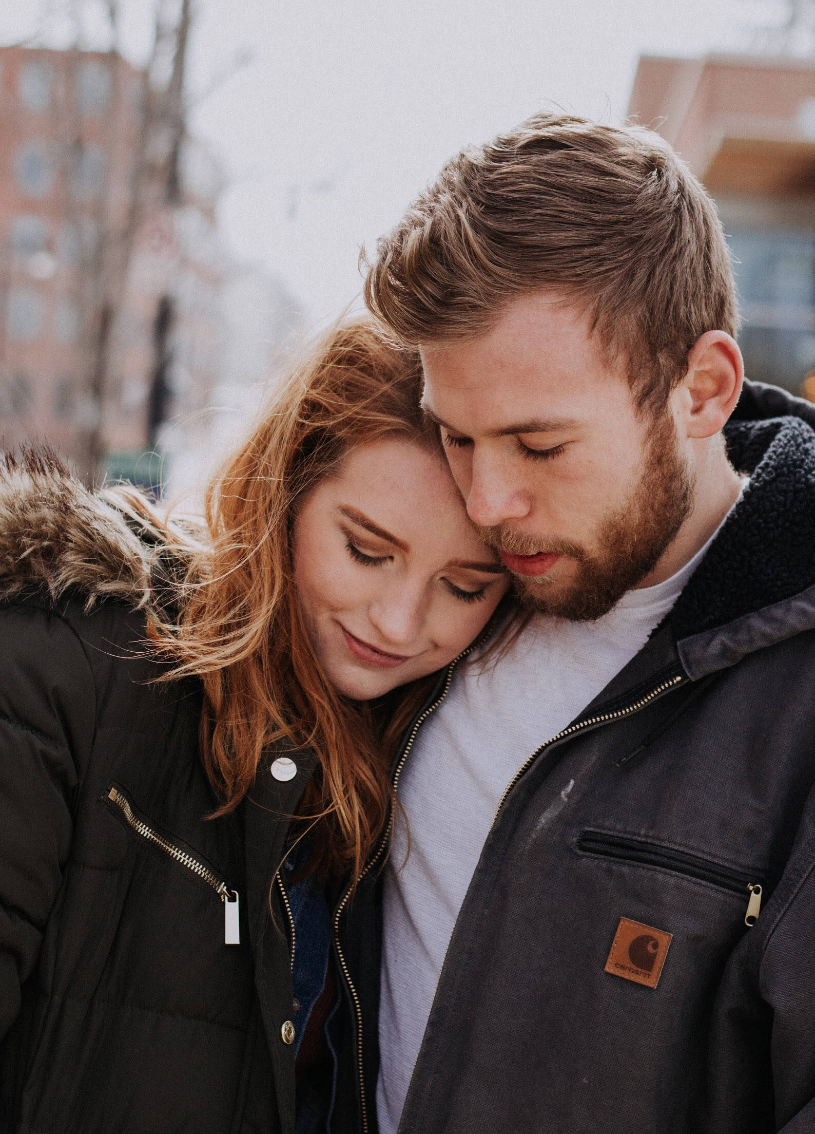 cute hug 桌布 壁紙 — 一對情侶在戶外穿著冬季外套，在模糊的城市背景下擁抱的溫柔時刻。