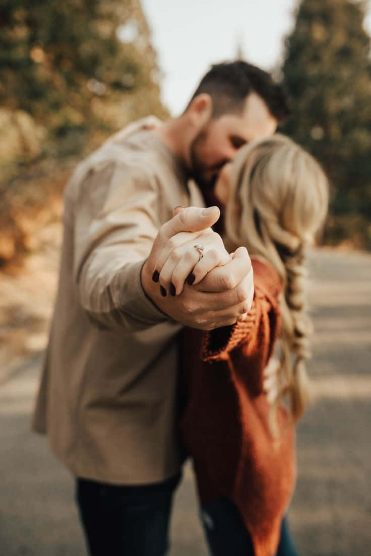 engagement 桌布 壁紙 — 一對情侶在戶外親吻，雙手在前景緊握。