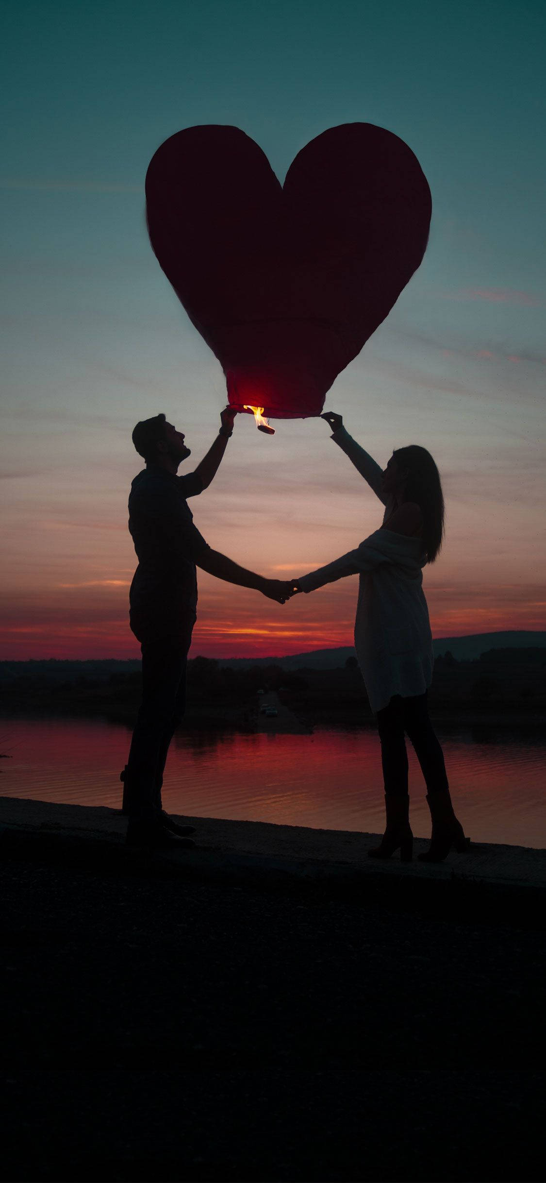 Love Story 桌布 壁紙 — 一對情侶在日落映襯下的剪影，在平靜的河上釋放一盞發光的愛心形燈籠。