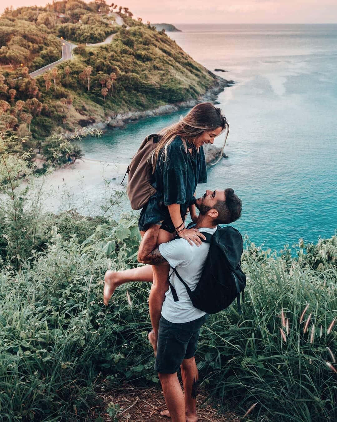 lover 桌布 壁紙 — 一對情侶在日落時分享受快樂時刻，男子在俯瞰碧綠海洋的懸崖上舉起女子。