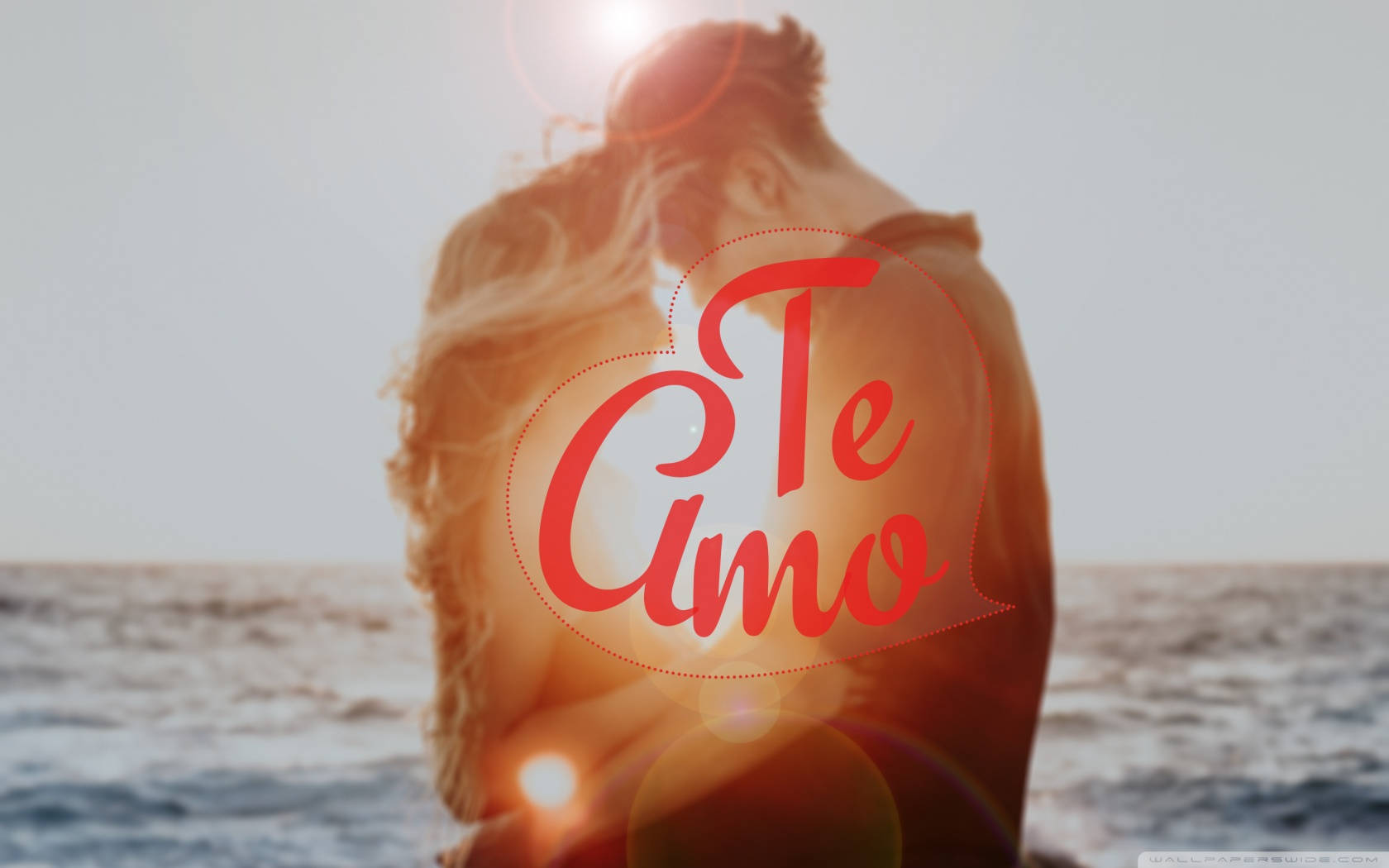 Te Amo 桌布 壁紙 — 一對情侶在日落時分的沙灘上擁抱，'Te Amo' 文字溫暖地閃耀在他們上方。