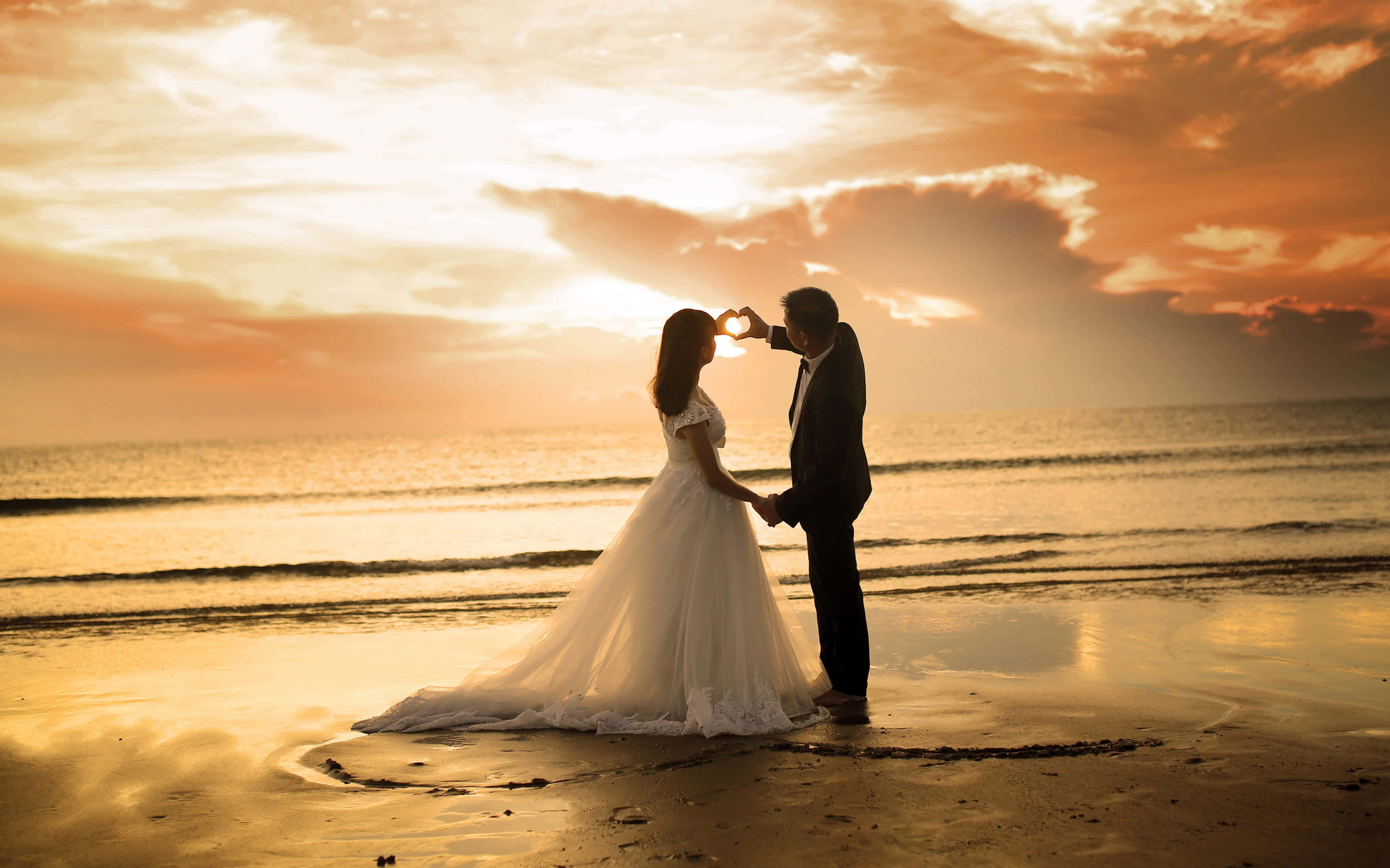 Wedding 桌布 壁紙 — 一對情侶在日落海灘上以剪影形式用手比出心形，同時互相擁抱。
