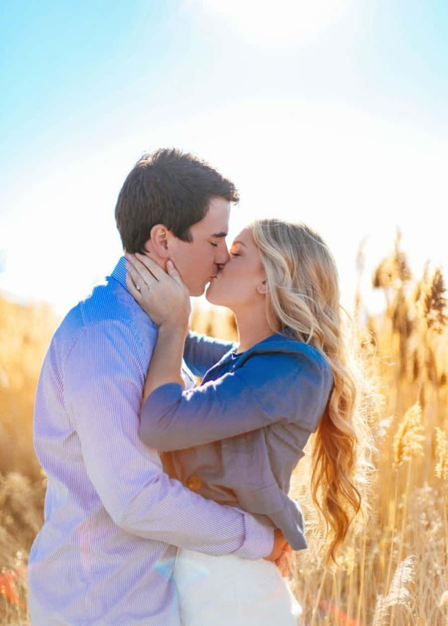 Kissing 桌布 壁紙 — 一對情侶在晴朗藍天下，於陽光明媚的金色蘆葦田中分享溫柔的親吻。