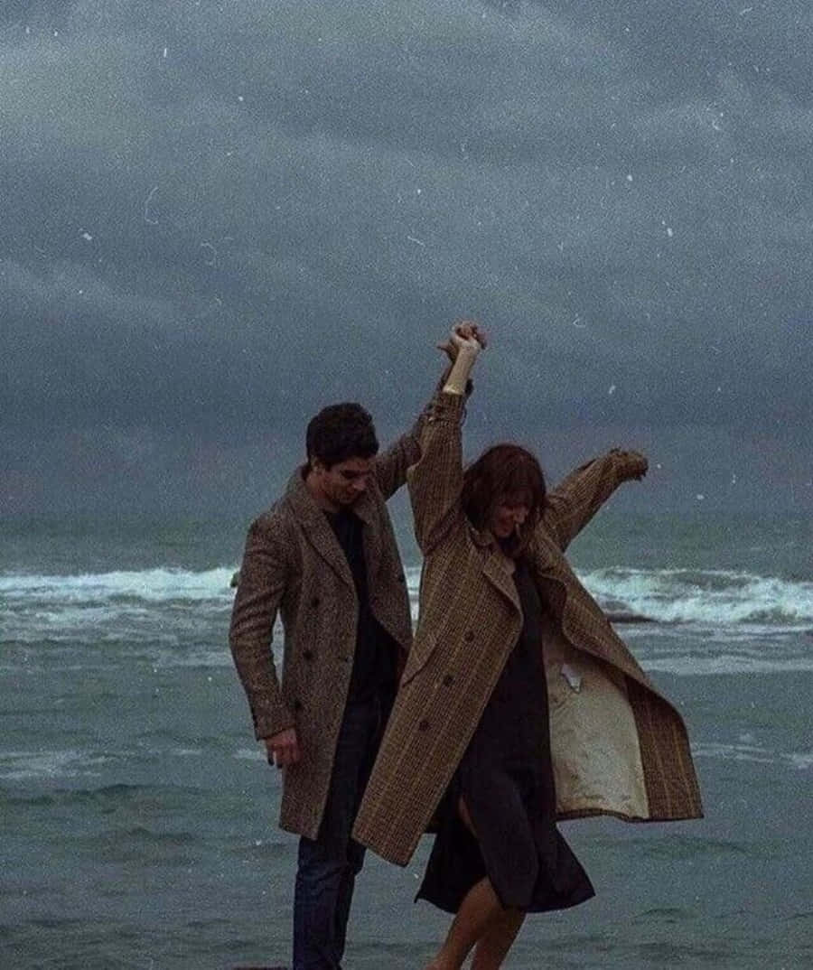 lover 桌布 壁紙 — 一對情侶在暴風雨的天空下，背後波濤洶湧，在雨中歡快地跳舞。