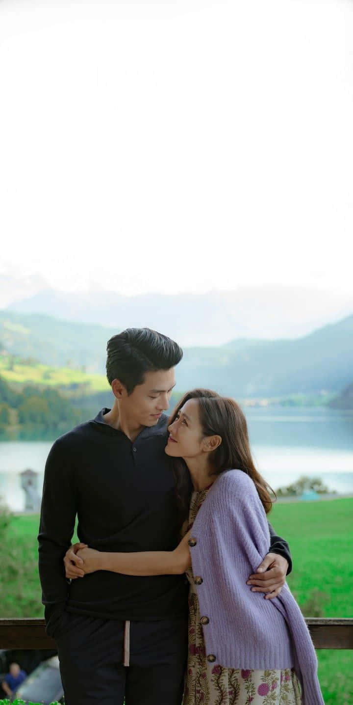 Couples 桌布 壁紙 — 一對情侶在木長椅上溫柔擁抱，俯瞰著寧靜的湖泊，背景是霧氣繚繞的山巒。