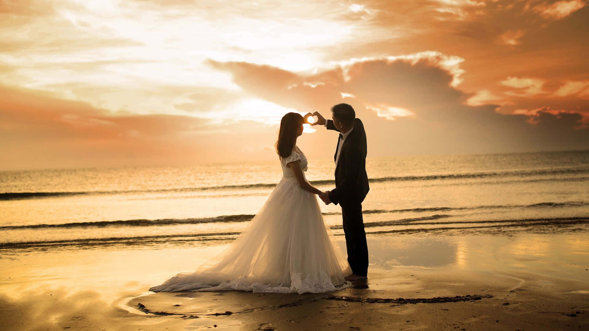 Beach Love 桌布 壁紙 — 一對情侶在沙灘上以剪影形式，在日落時用手圍著太陽形成心形。