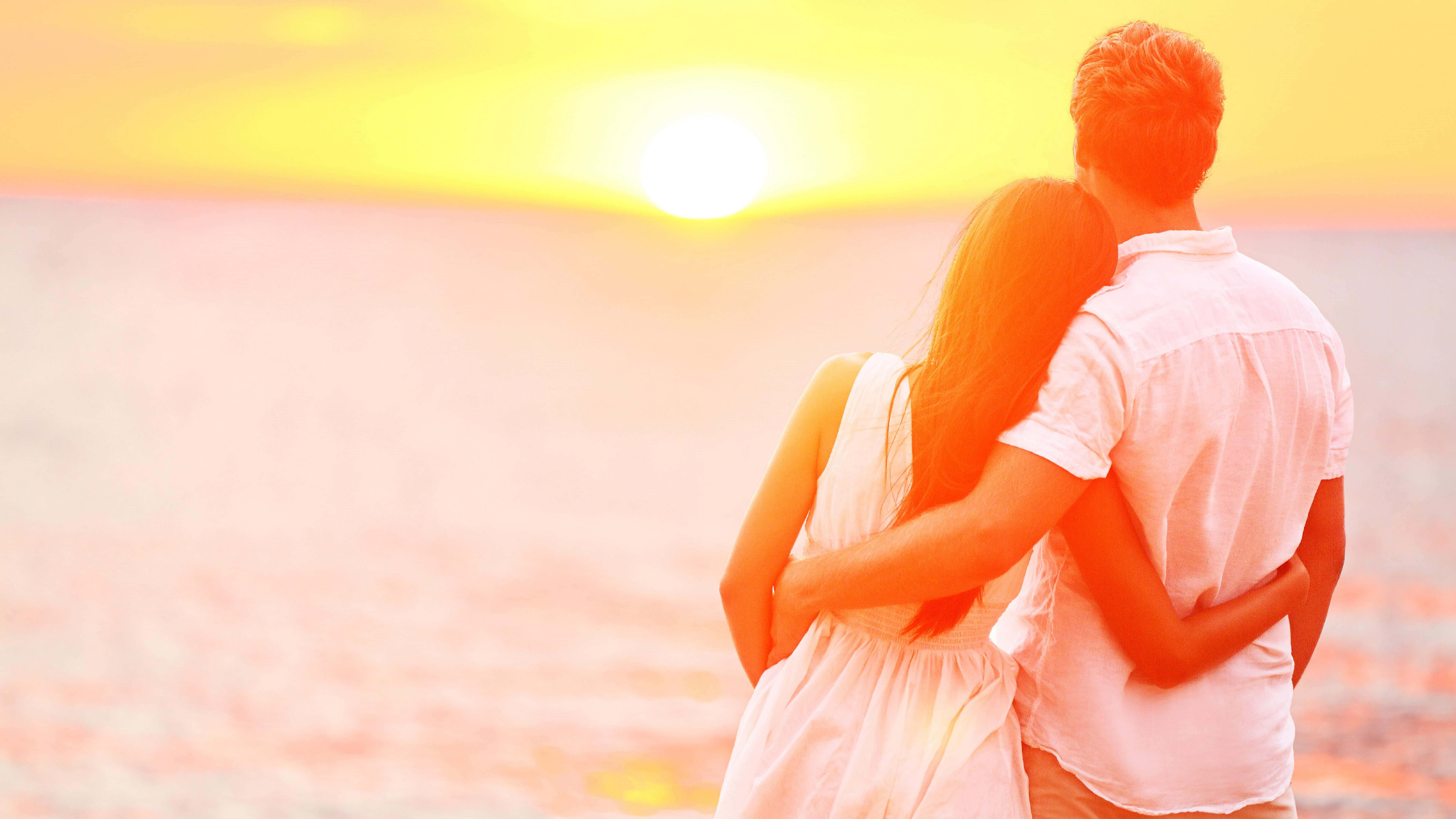 couple love 桌布 壁紙 — 一對情侶在沙灘上擁抱，夕陽以溫暖的金色色調沉入海洋。