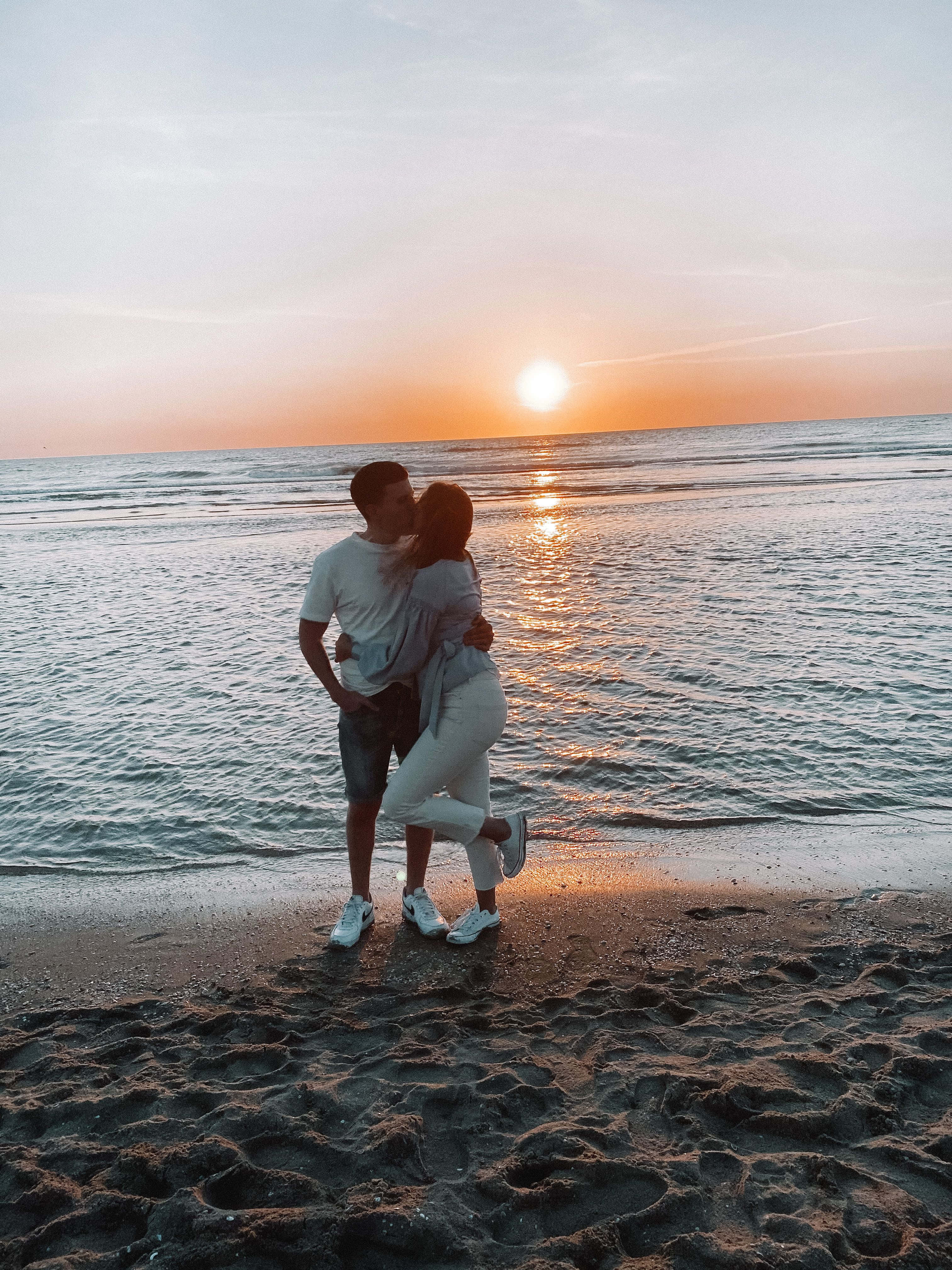 海灘 桌布 壁紙 — 一對情侶在沙灘上擁抱，夕陽在海面上灑下金色光芒。
