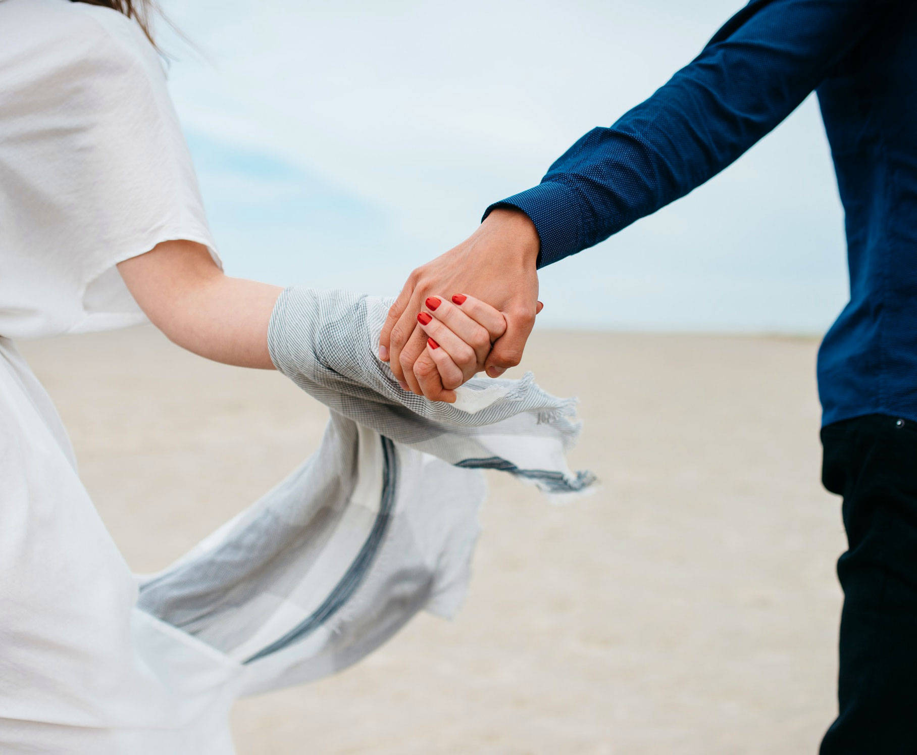 hand 桌布 壁紙 — 一對情侶在沙灘上牽手，微風吹起女士飄逸的圍巾。