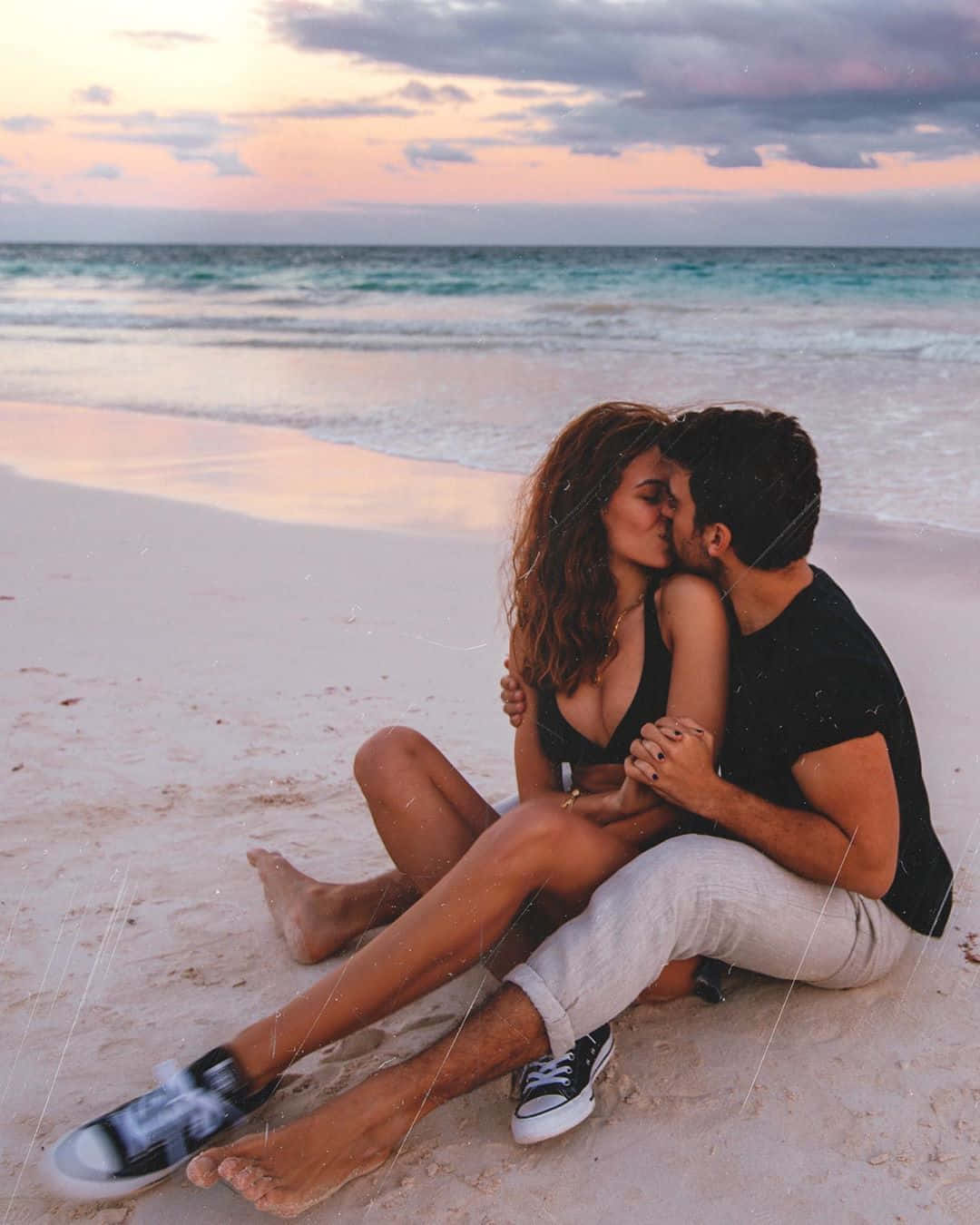 couple kiss 桌布 壁紙 — 一對情侶在沙灘上親吻，背景是日落、碧綠海浪和粉紅雲彩。