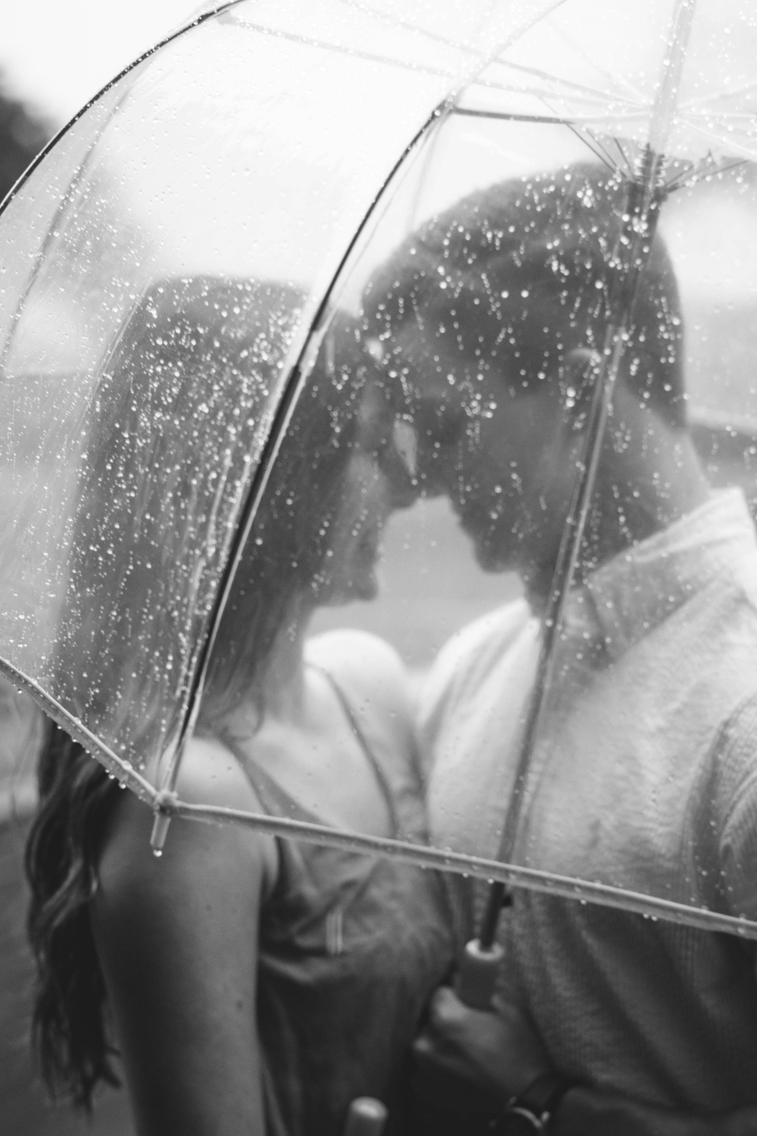 黑白 桌布 壁紙 — 一對情侶在沾滿雨滴的透明雨傘下接吻的黑白親密時刻。