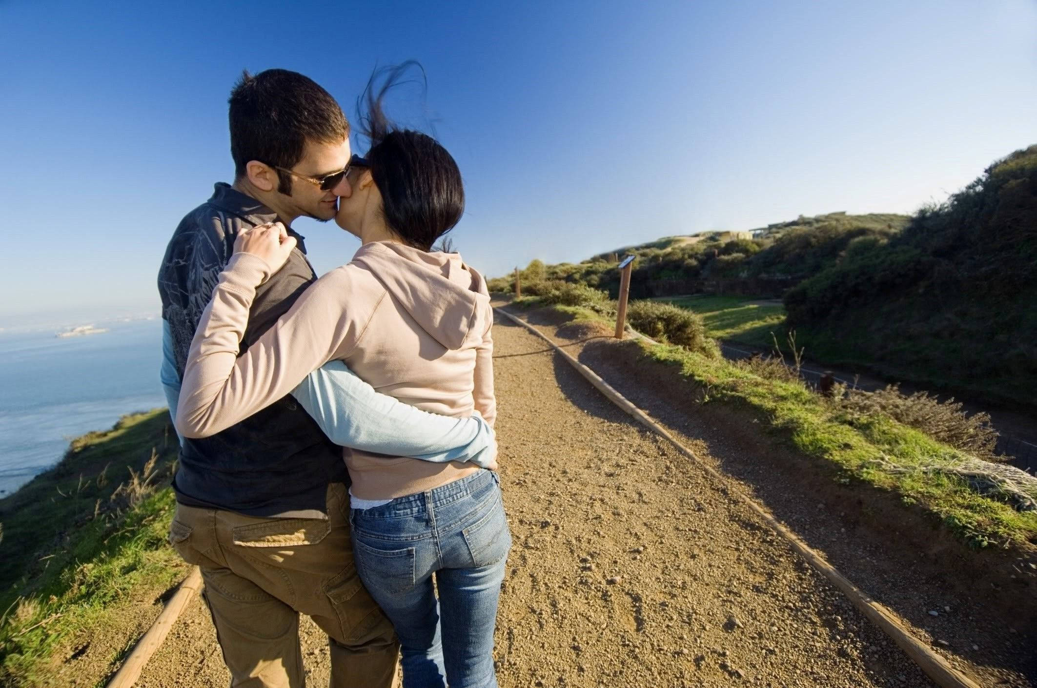 Romantic Love 桌布 壁紙 — 一對情侶在沿海小徑上熱情接吻，欣賞海洋美景和晴朗藍天。