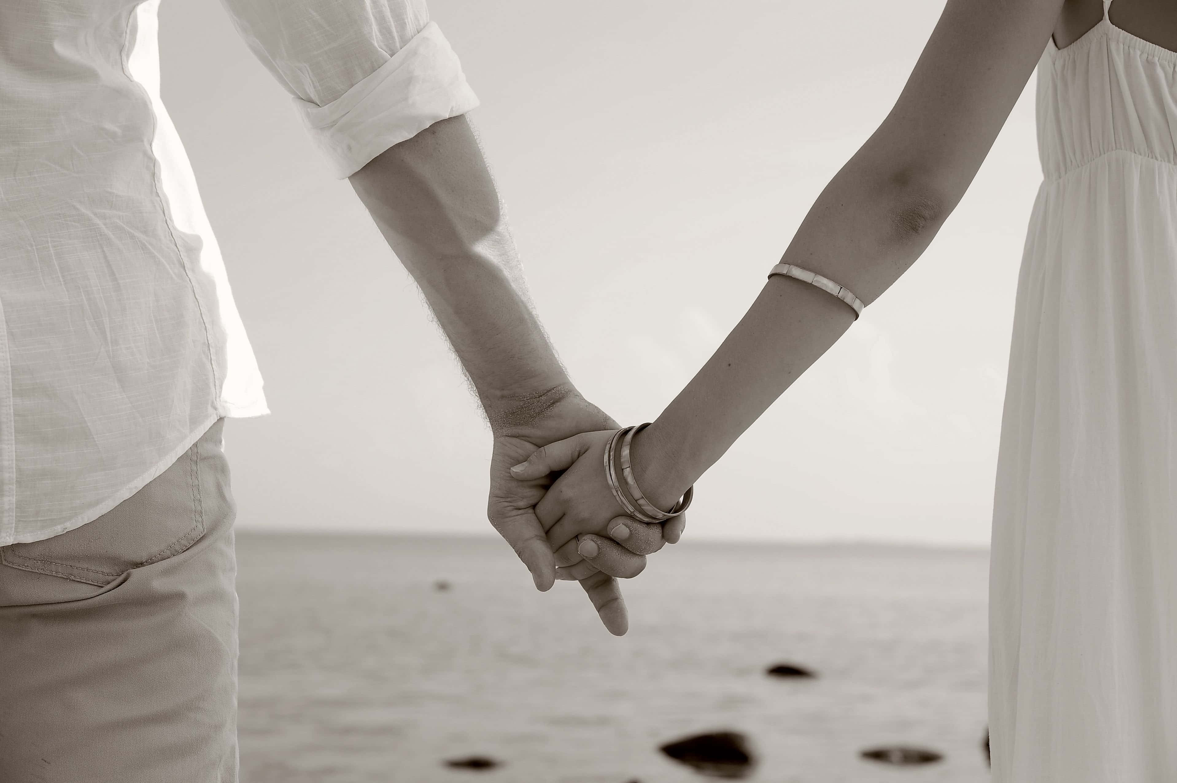 Couple Holding Hand 桌布 壁紙 — 一對情侶在海邊牽手，柔和的懷舊色調，有溫柔的海浪和遠處的地平線。