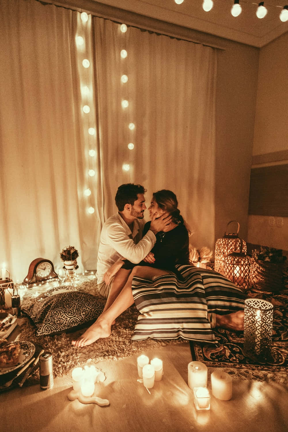Relationship 桌布 壁紙 — 一對情侶在溫暖照明的房間裡，在舒適的地毯上親吻，周圍環繞著燈串和閃爍的蠟燭。