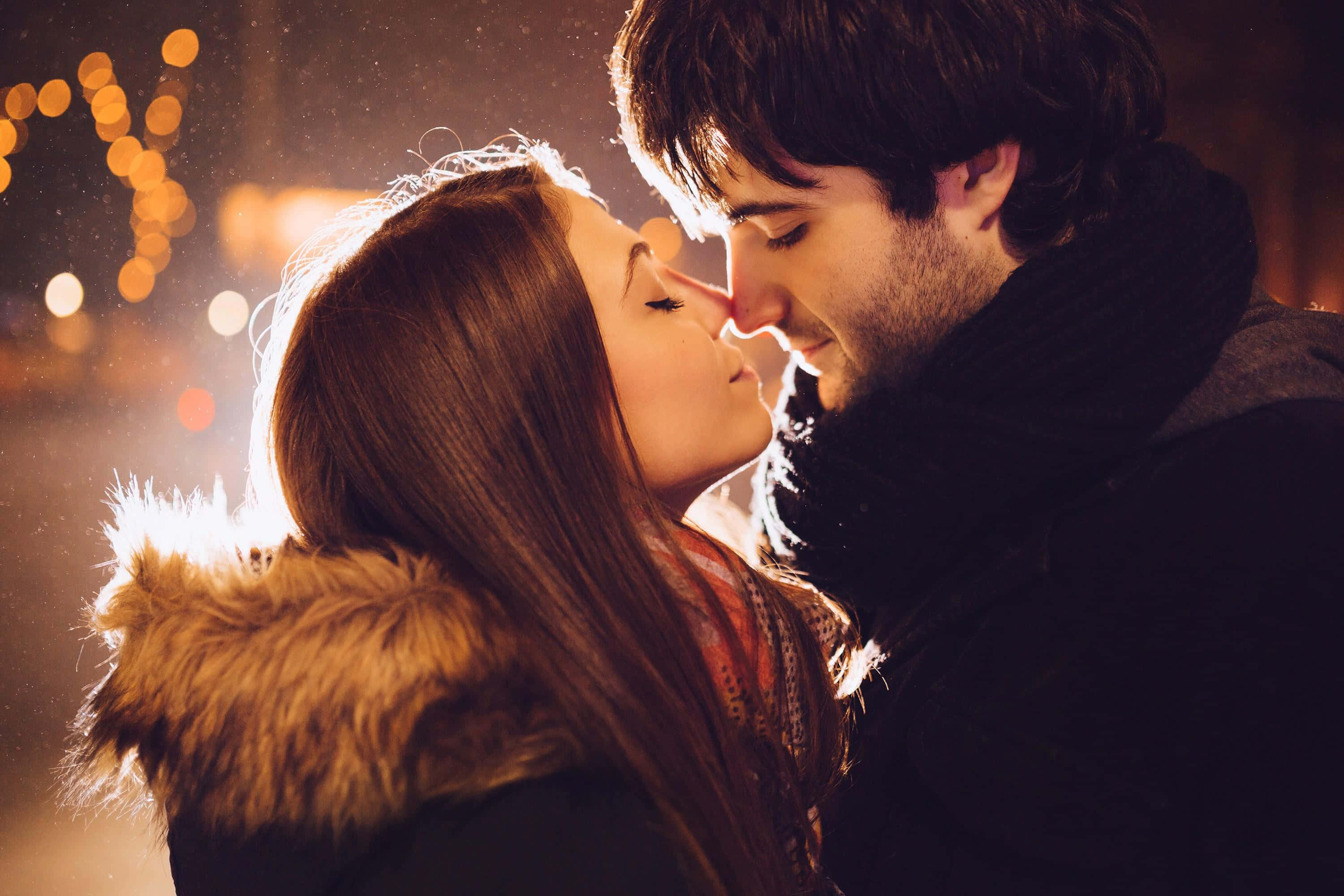 Beautiful Couple 桌布 壁紙 — 一對情侶在溫暖燈光、雪花紛飛的城市夜景中，鼻尖對鼻尖分享親密時刻，背景有散景燈光。