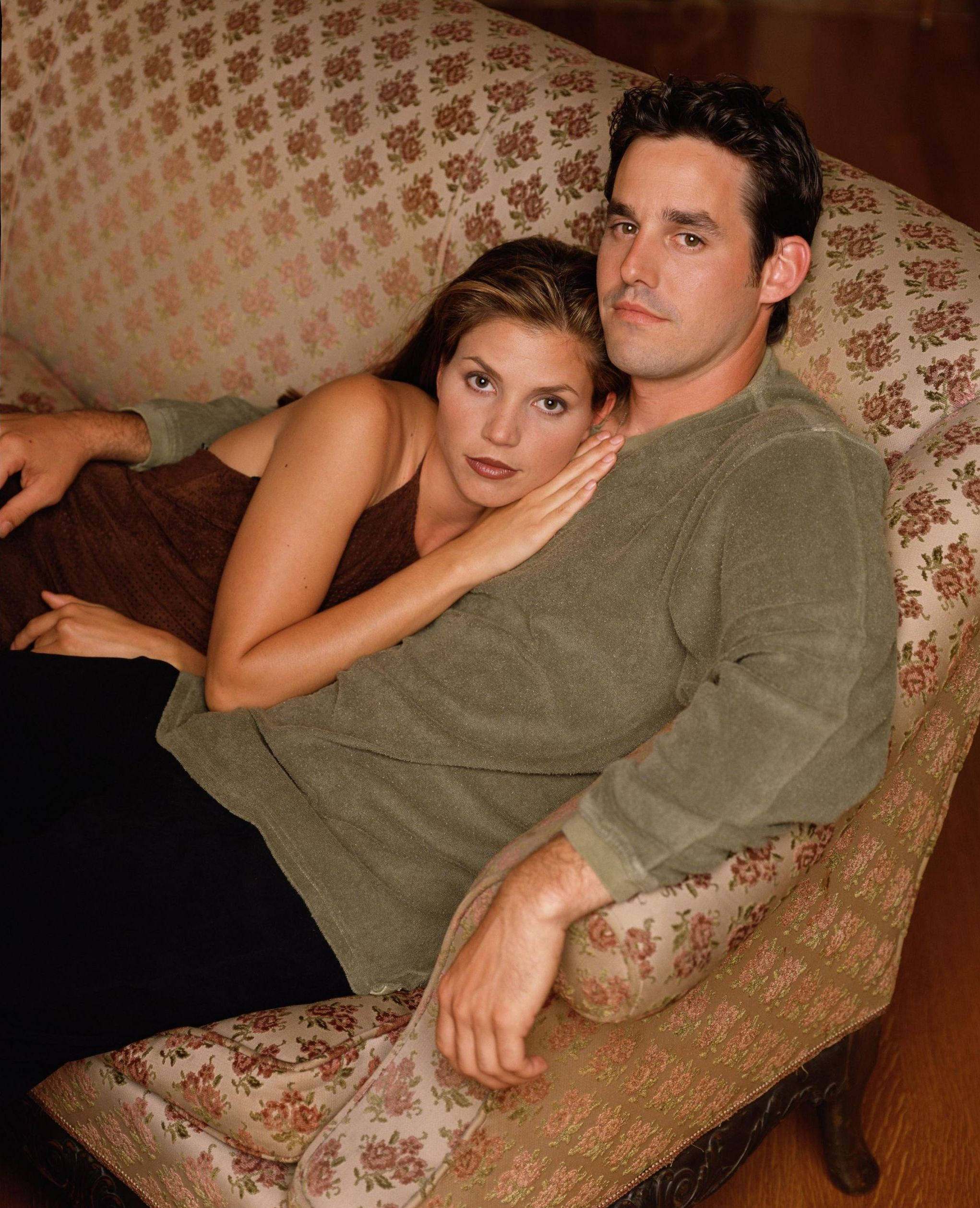 Nicholas Brendon 桌布 壁紙 — 一對情侶在溫暖燈光的室內環境中，親密地躺在花卉圖案的沙發上。
