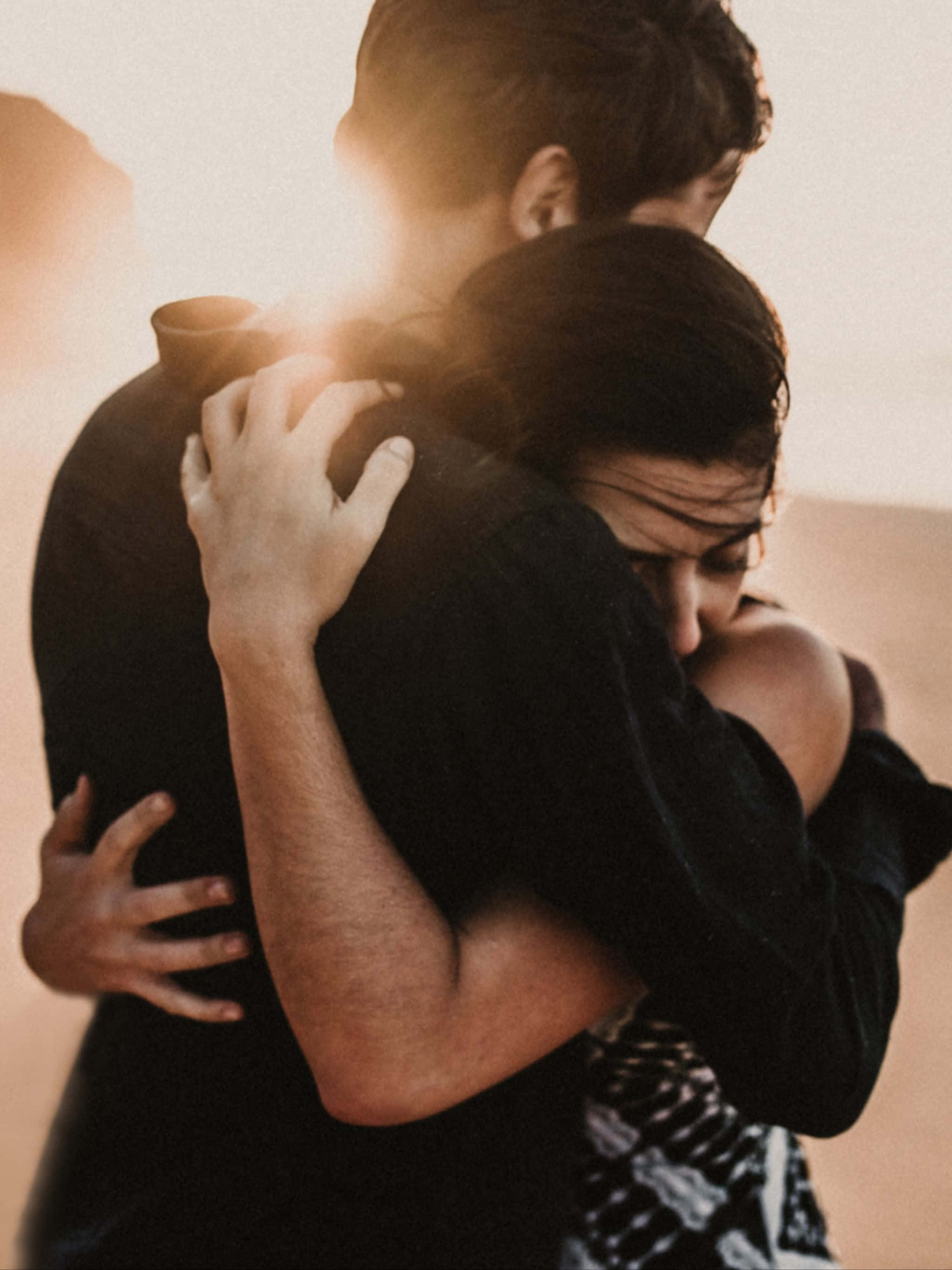 Hugging 桌布 壁紙 — 一對情侶在溫暖燦爛的日落背景下緊緊擁抱，柔和的金色光線穿過。