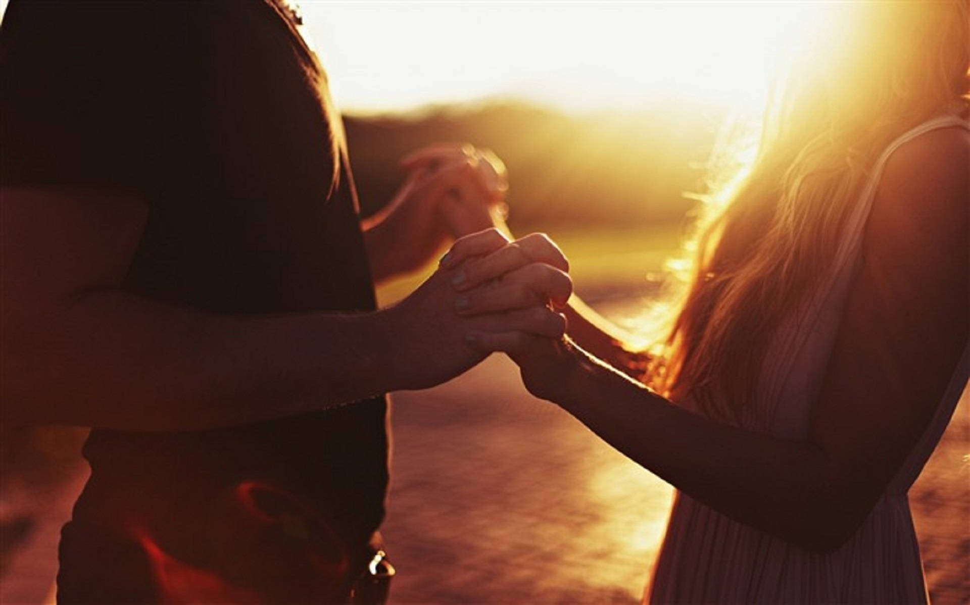 Romantic Love 桌布 壁紙 — 一對情侶在溫暖的金色日落光線中牽手，背景有剪影人物和發光的逆光。