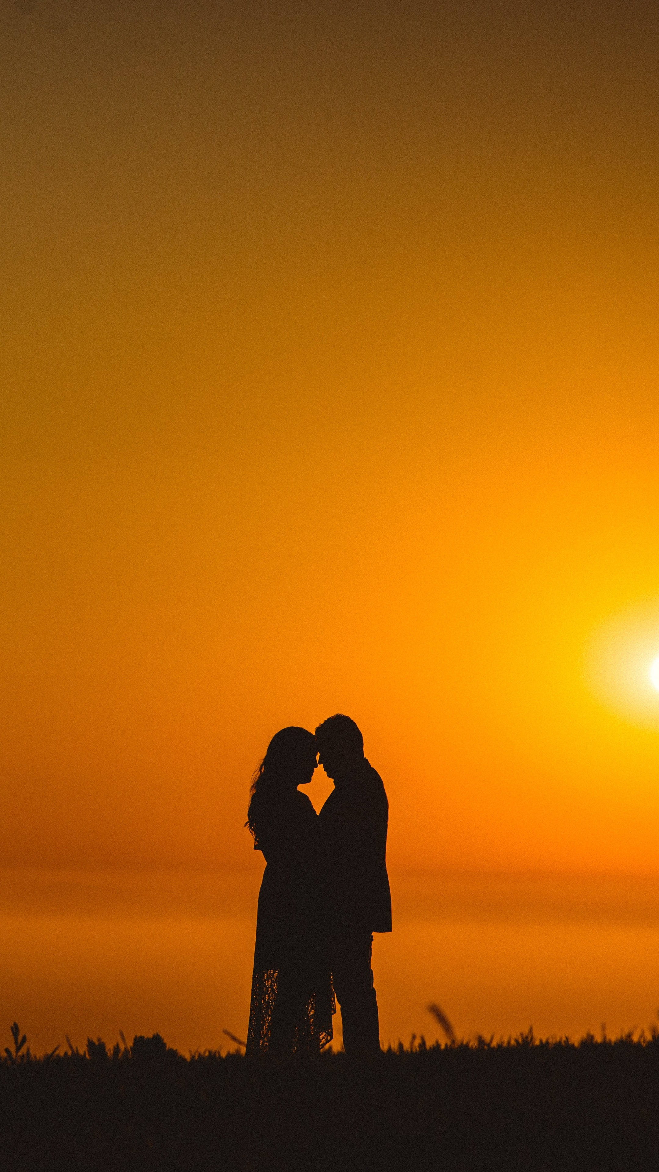 2160x3840 桌布 壁紙 — 一對情侶在火紅橙色夕陽天空下擁抱的浪漫剪影。