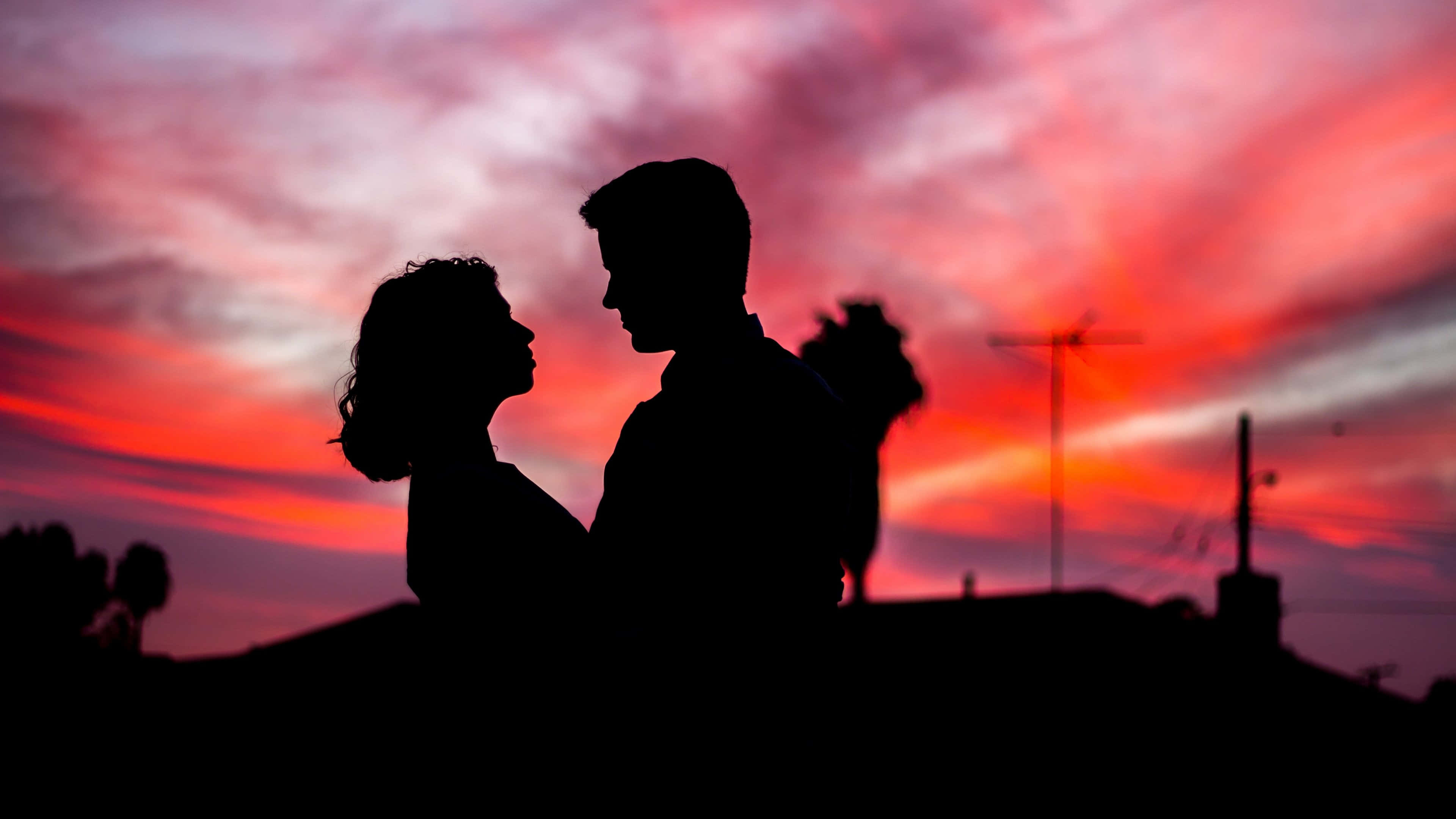 couple love 桌布 壁紙 — 一對情侶在熾熱的日落天空下凝視對方眼睛的浪漫剪影。
