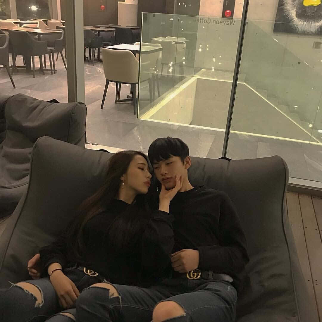 Couples 桌布 壁紙 — 一對情侶在現代休息室的灰色沙發上親密依偎，休息室有玻璃牆和昏暗燈光。