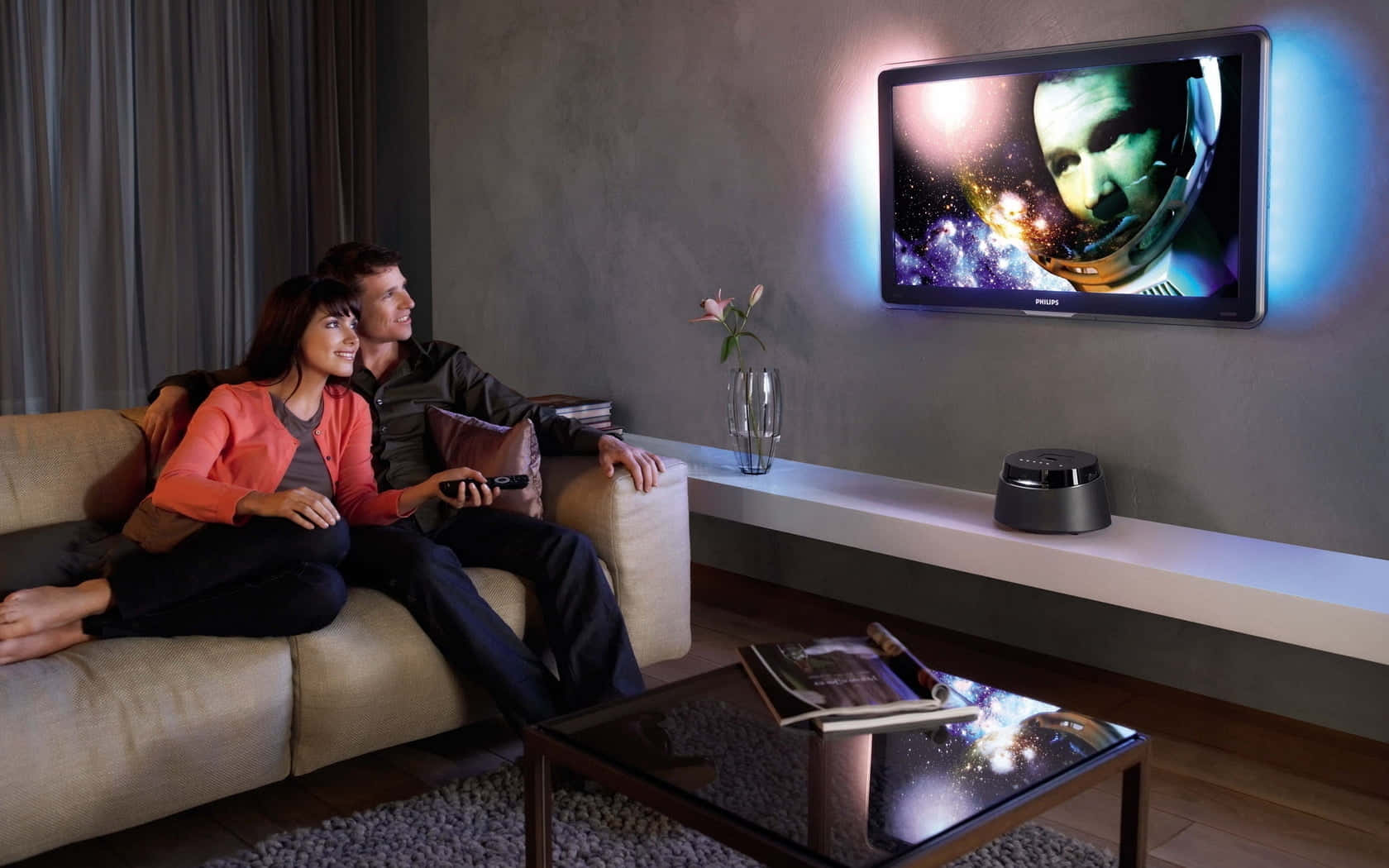 Home Entertainment 桌布 壁紙 — 一對情侶在現代客廳的米色沙發上放鬆，觀看壁掛電視上的宇宙電影，伴隨著藍色環境燈光。