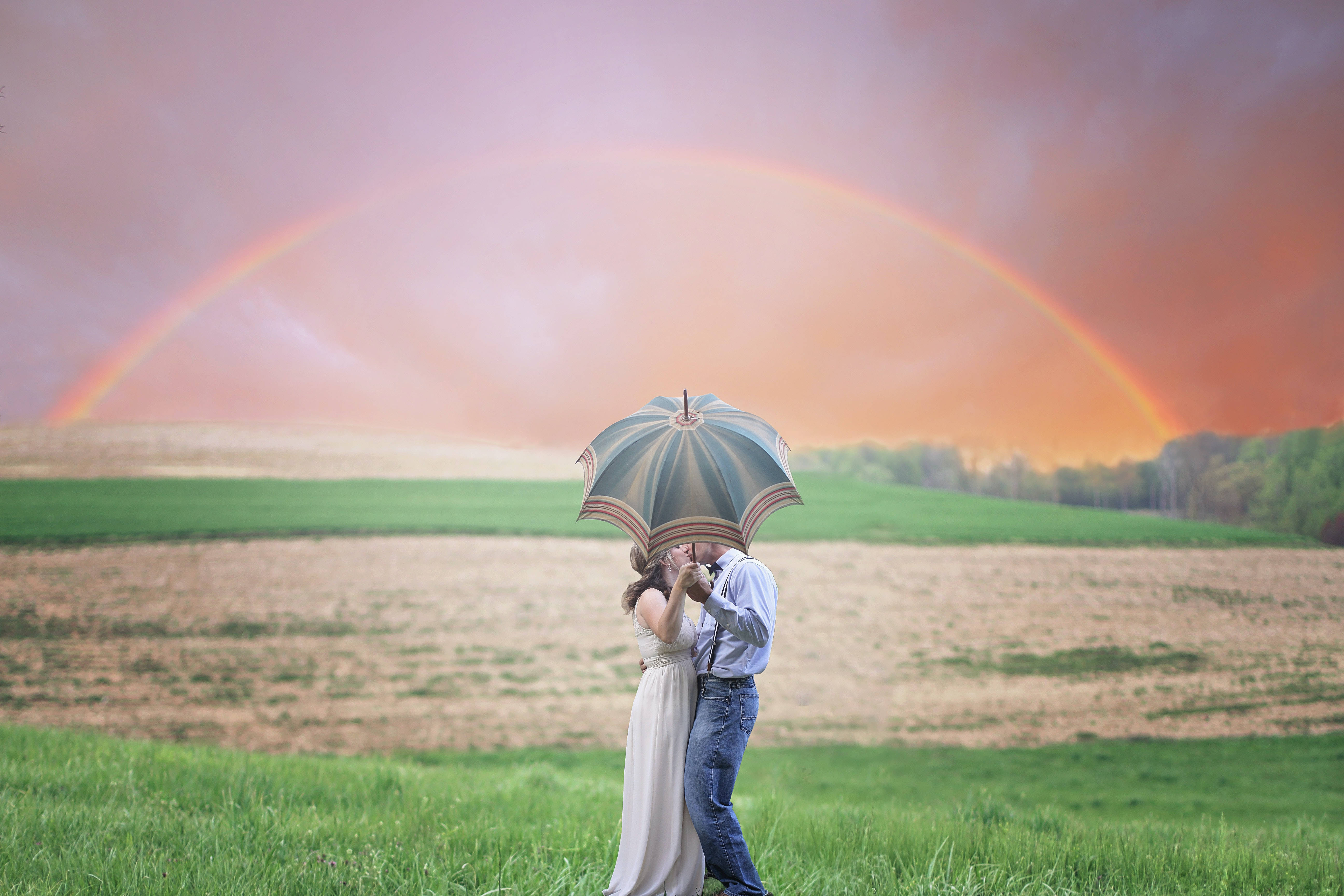 Romantic Love 桌布 壁紙 — 一對情侶在田野中，於圖案雨傘下接吻，一道鮮豔的彩虹橫跨夕陽天空。