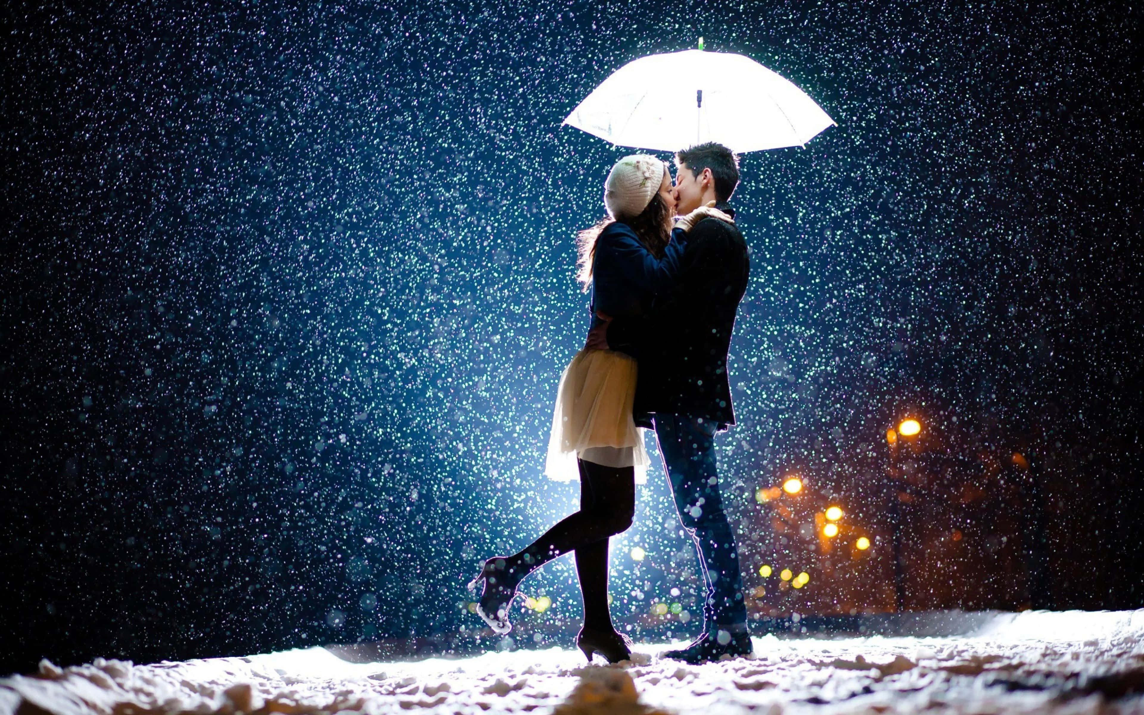 Sweet Love 桌布 壁紙 — 一對情侶在發光的白色雨傘下接吻，雪花在黑暗的夜空下飄落，背景是溫暖的路燈。