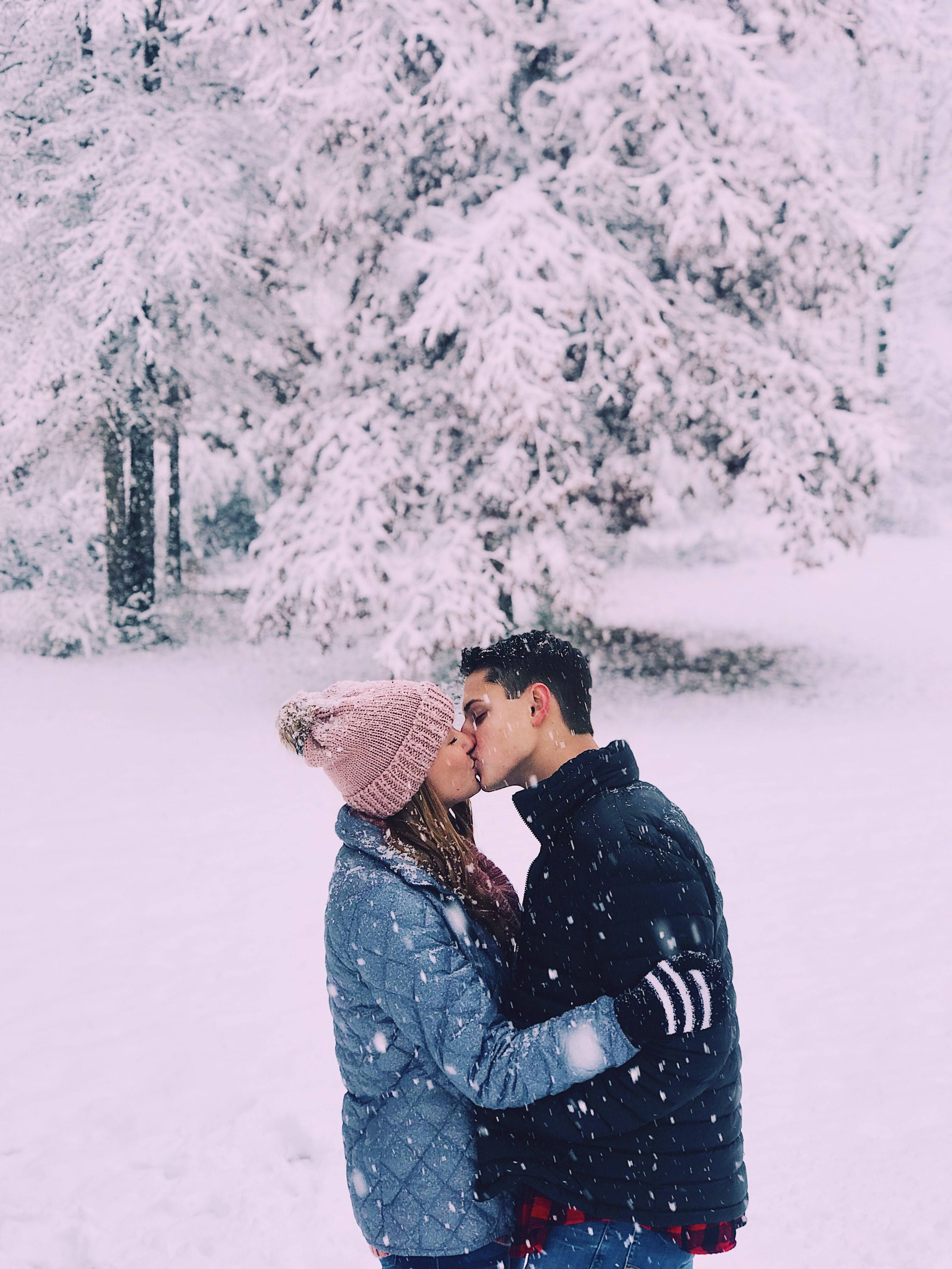 Love Story 桌布 壁紙 — 一對情侶在白雪覆蓋的森林中親吻，周圍是積雪的樹木和飄落的雪花。