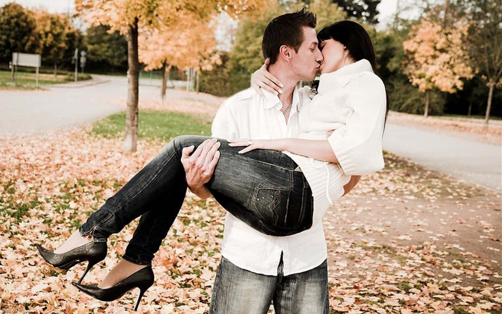 Kissing 桌布 壁紙 — 一對情侶在秋天的公園裡熱情接吻，落葉鋪滿了他們周圍的地面。