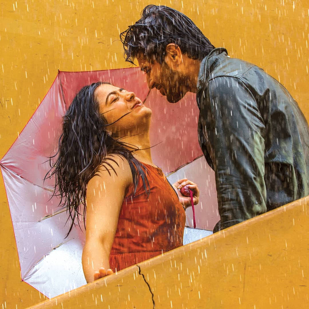 vijay devarakonda 4K 桌布 壁紙 — 一對情侶在紅色雨傘下分享親密時刻，雨水打在溫暖的黃色牆上。