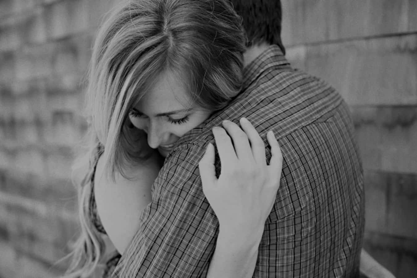 Hug 桌布 壁紙 — 一對情侶在紋理磚牆前，柔和燈光下的溫柔黑白擁抱。